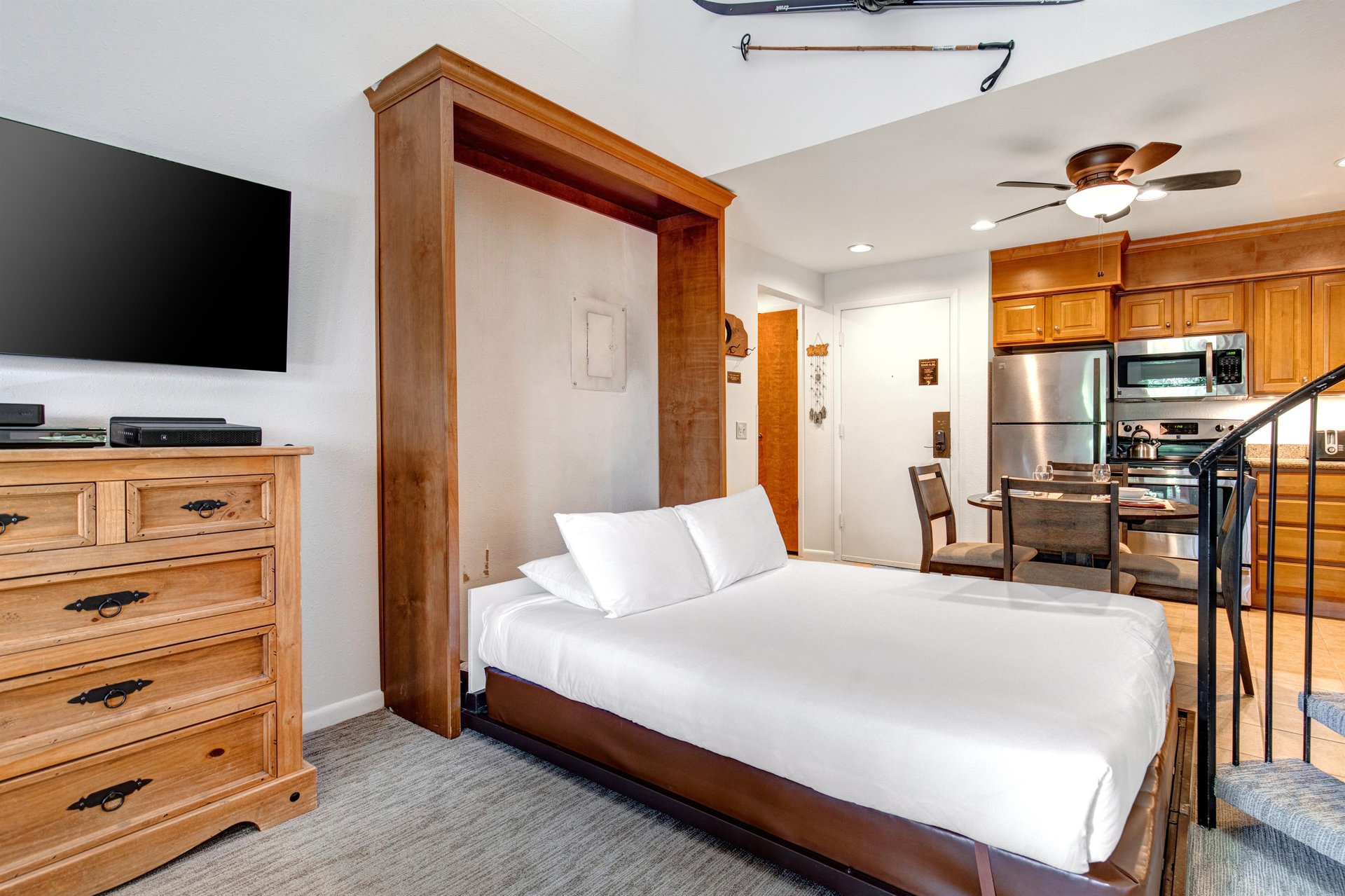 Snow Flower 31s living room with a Murphy Bed made with white linens, wood dresser, and wall mounted TV above it.