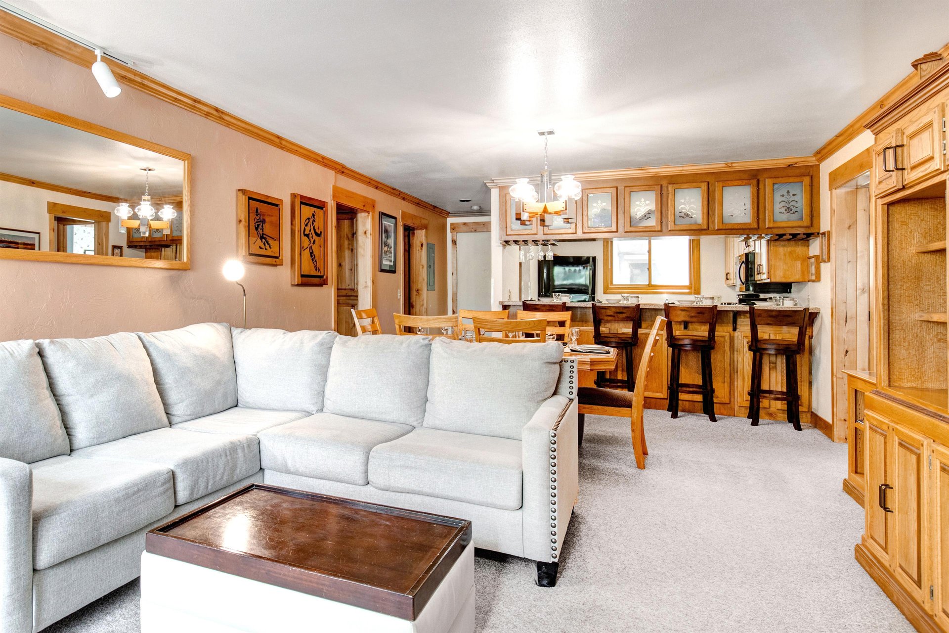 Snow Flower 43s living room looks into the dining area and kitchen and has cream colored carpet and wood trim.