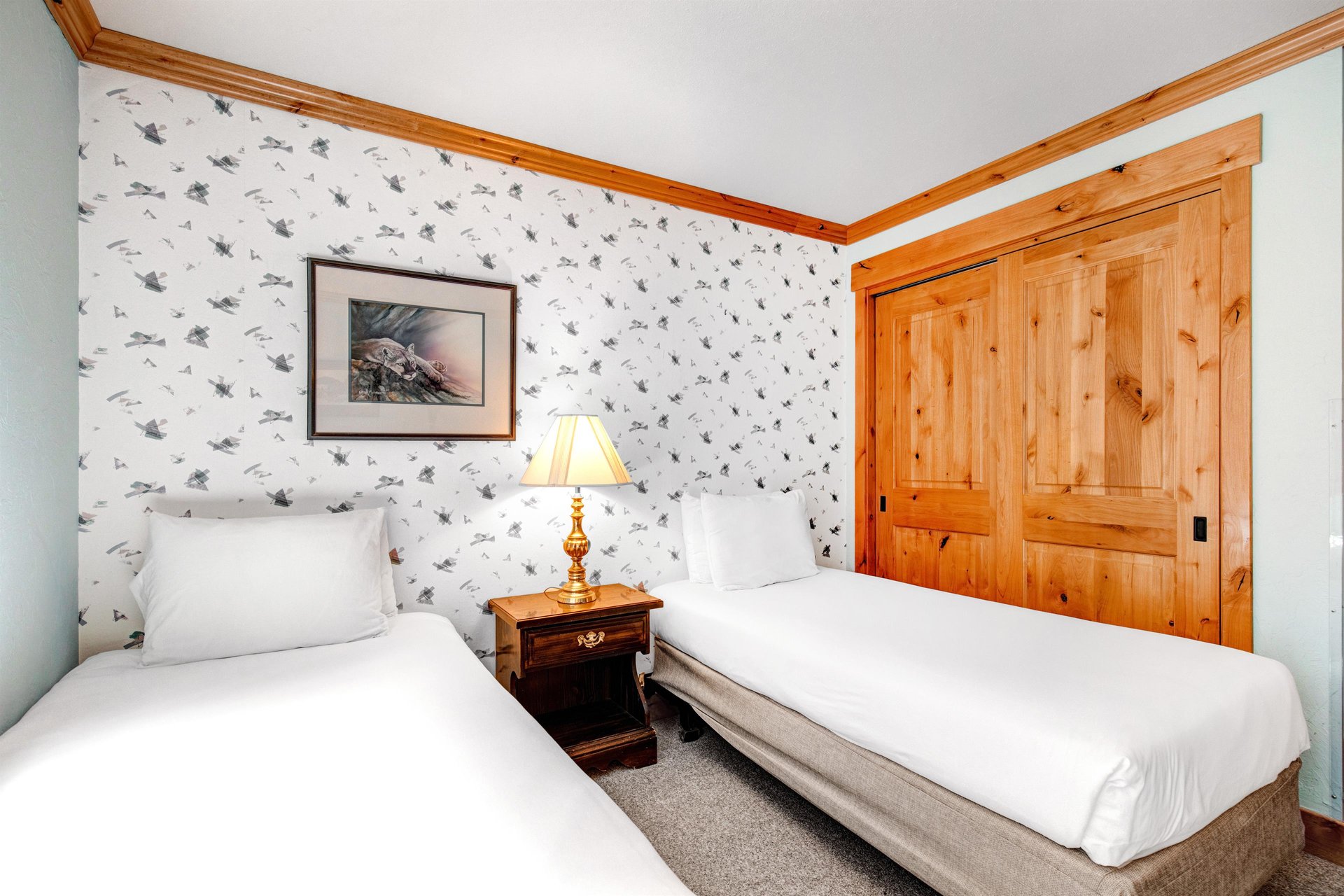 Snow Flower 43s third bedroom has 2 twin beds, one dresser and lamp in the middle, and white wallpaper on an accent wall.