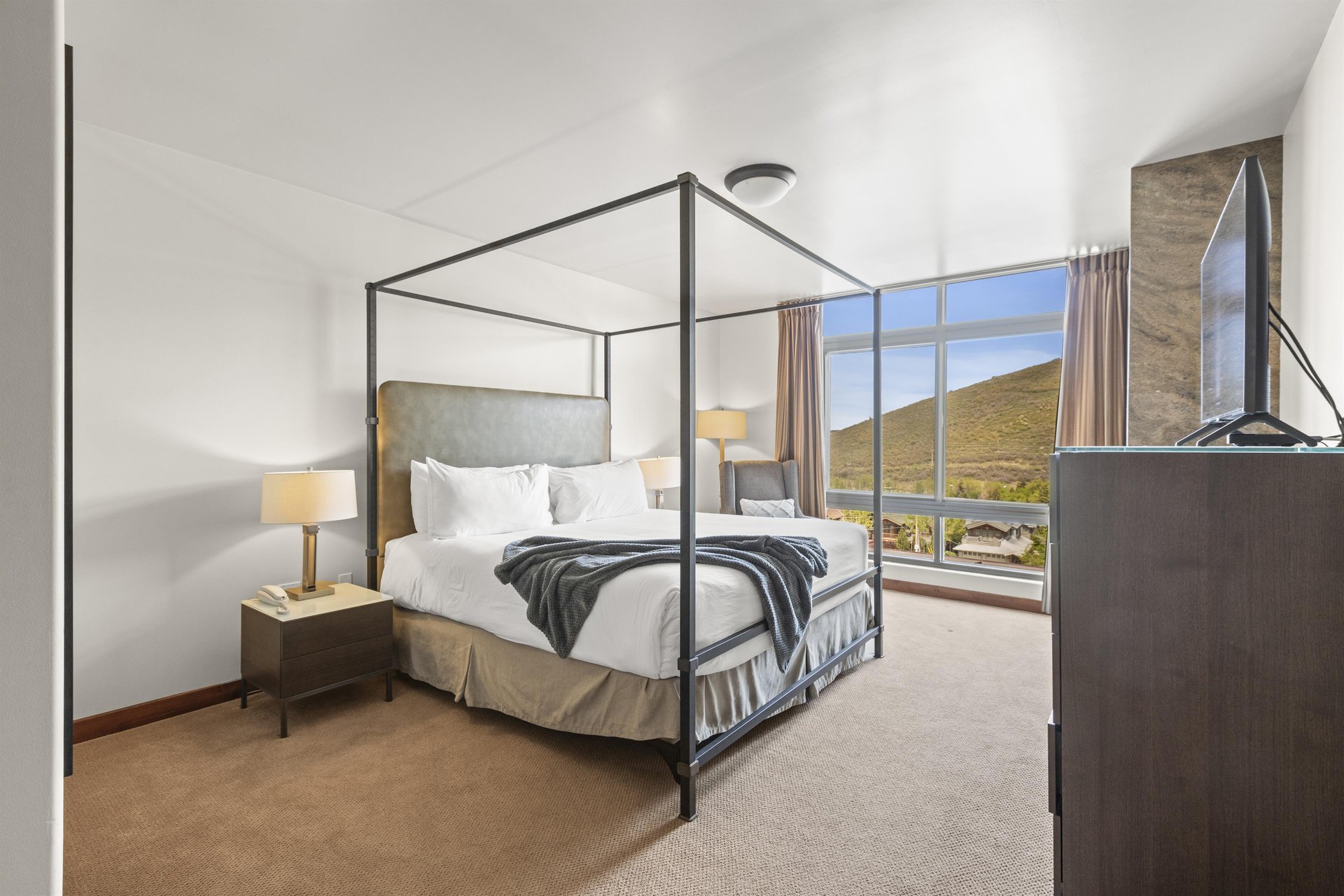The main suite has a king size bed and is next to floor to ceiling windows that have floor to ceiling drapes.