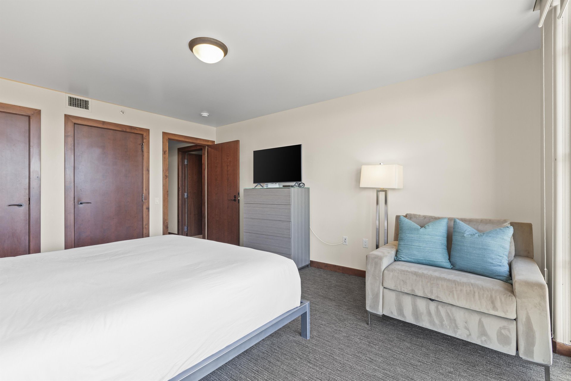 The third bedroom has a king size bed, grey dresser with TV on top, and a oversized comfy chair.