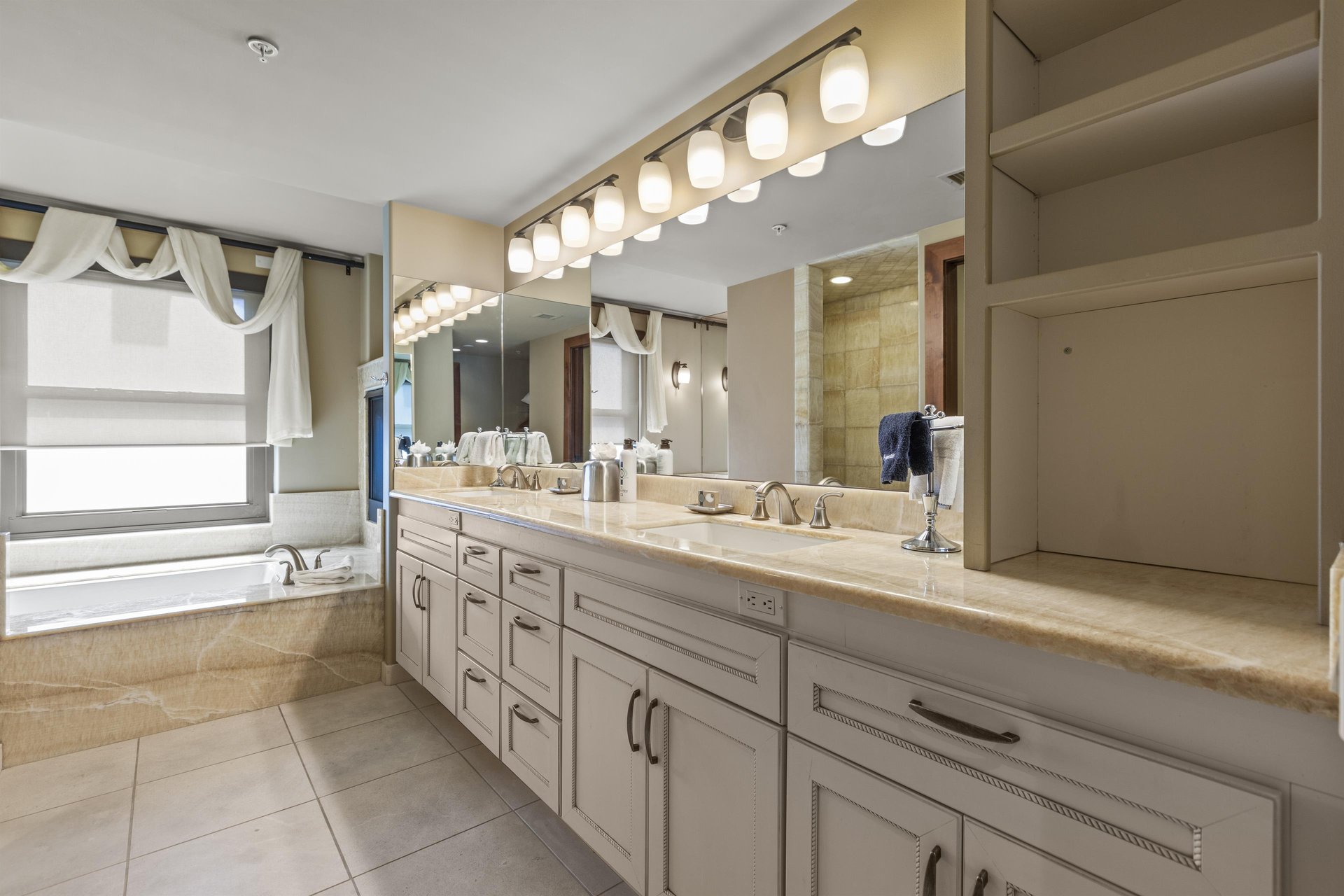 The second bedrooms en suite bathroom has a large two sink vanity, mirror, and lighting.