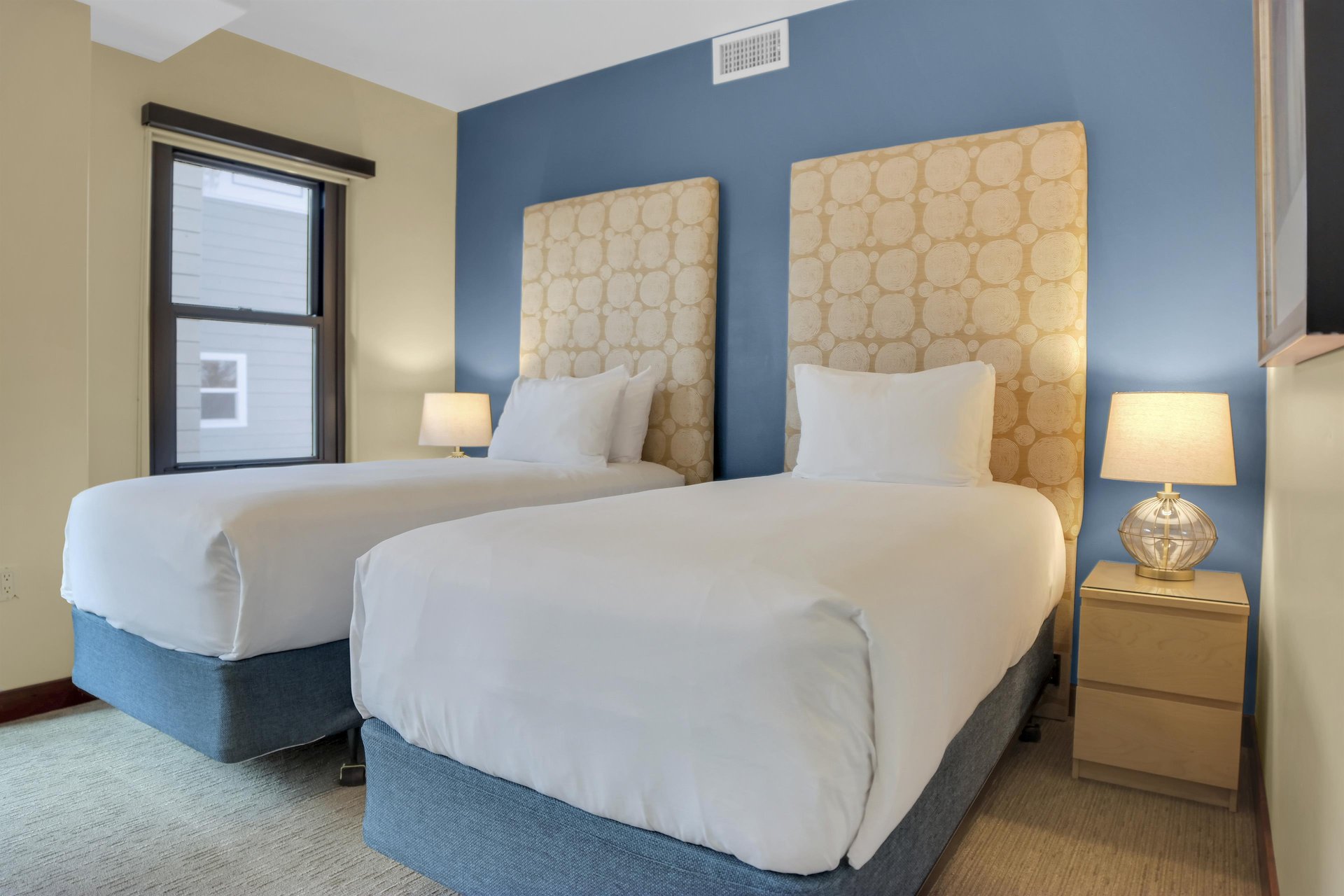 Lowell 304s second bedroom with two twin beds that have a large upholstered headboard and blue accent wall.