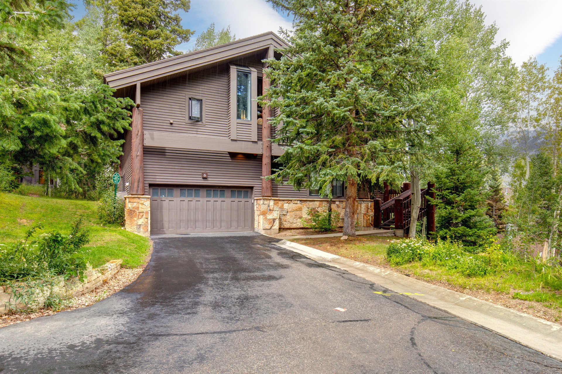 The Aspen Hollow 6 exterior is surrounded by green grass, trees, and other flowering plants.