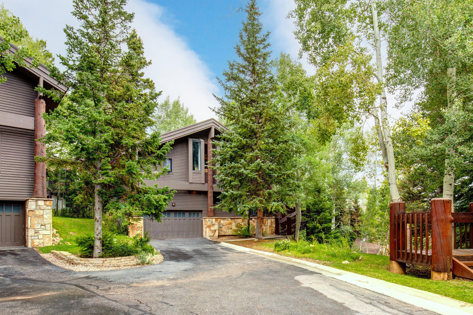 The Aspen Hollow 6 exterior is surrounded by green grass, trees, and other flowering plants.