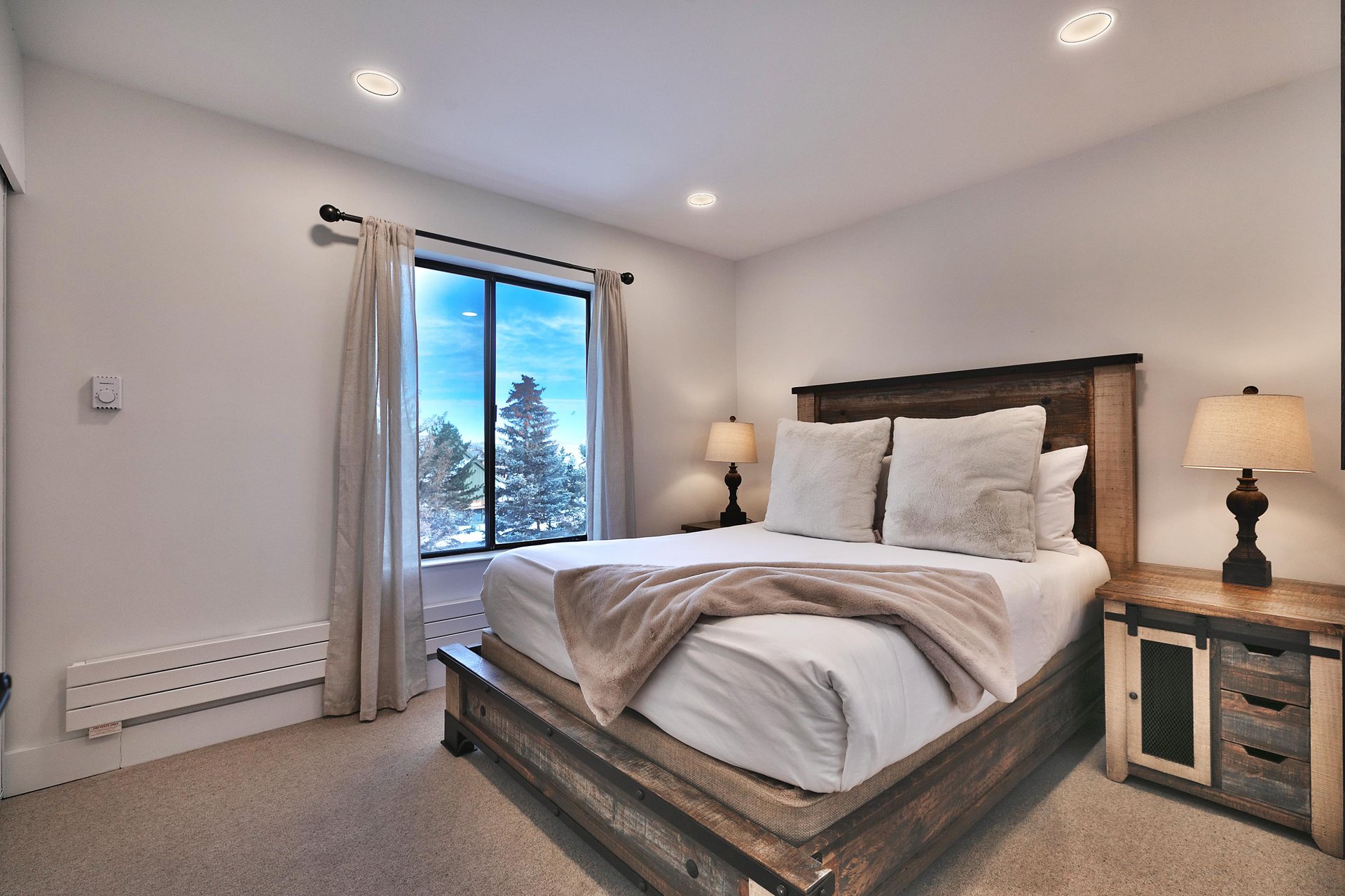 Main bedroom with queen bed and wooden bedframe with large picture window