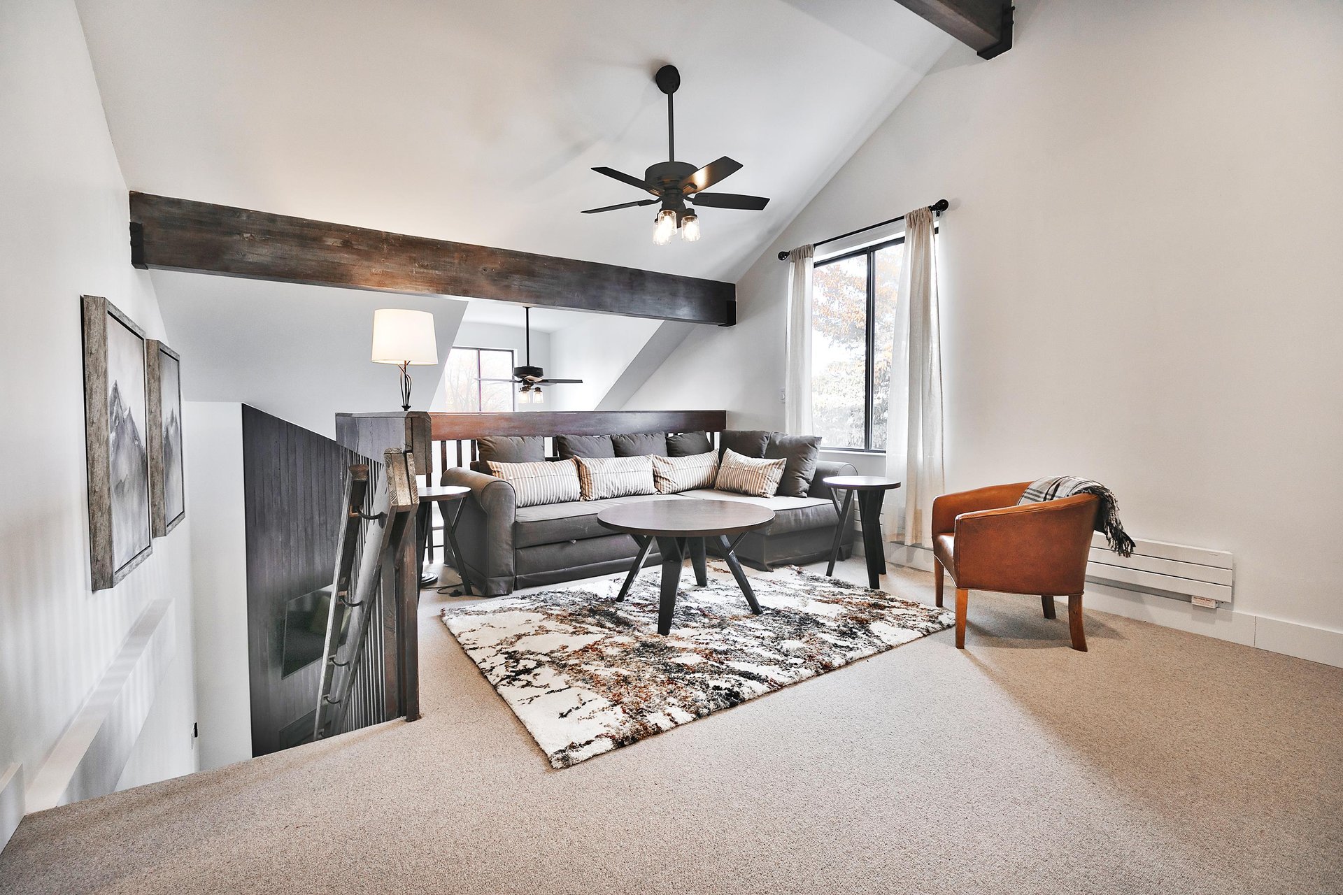 Loft area with large gray sectional, brown leather barrel accent chair and large picture window