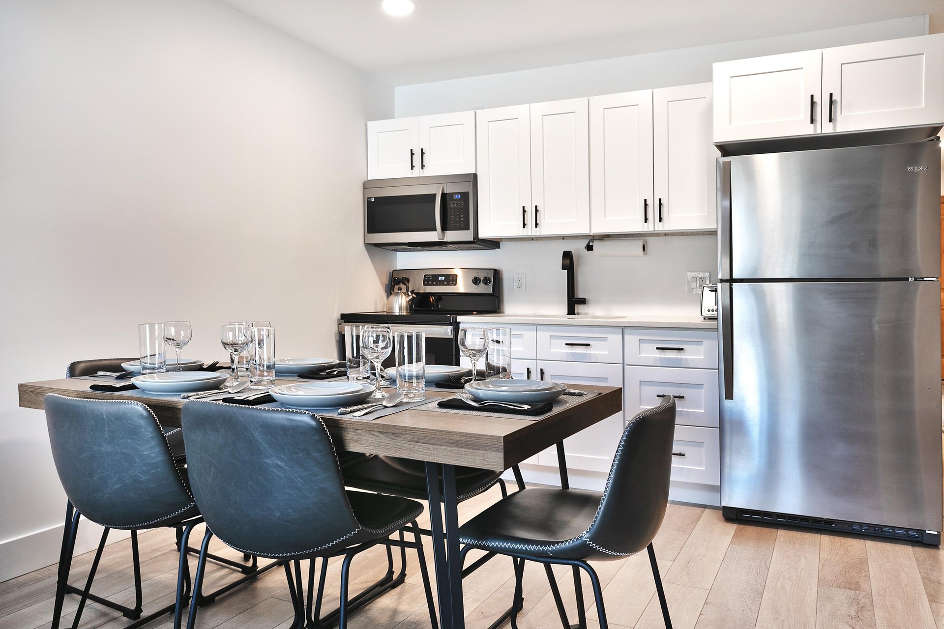 Dining room with wooden table, gray leather barrel dining room chairs, and kitchen in the background