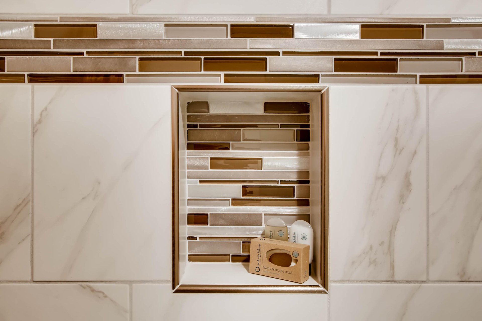 The shared bathroom has gorgeous white tile, with gold and brown decorative tile lining a shelf in the bathtub surround.