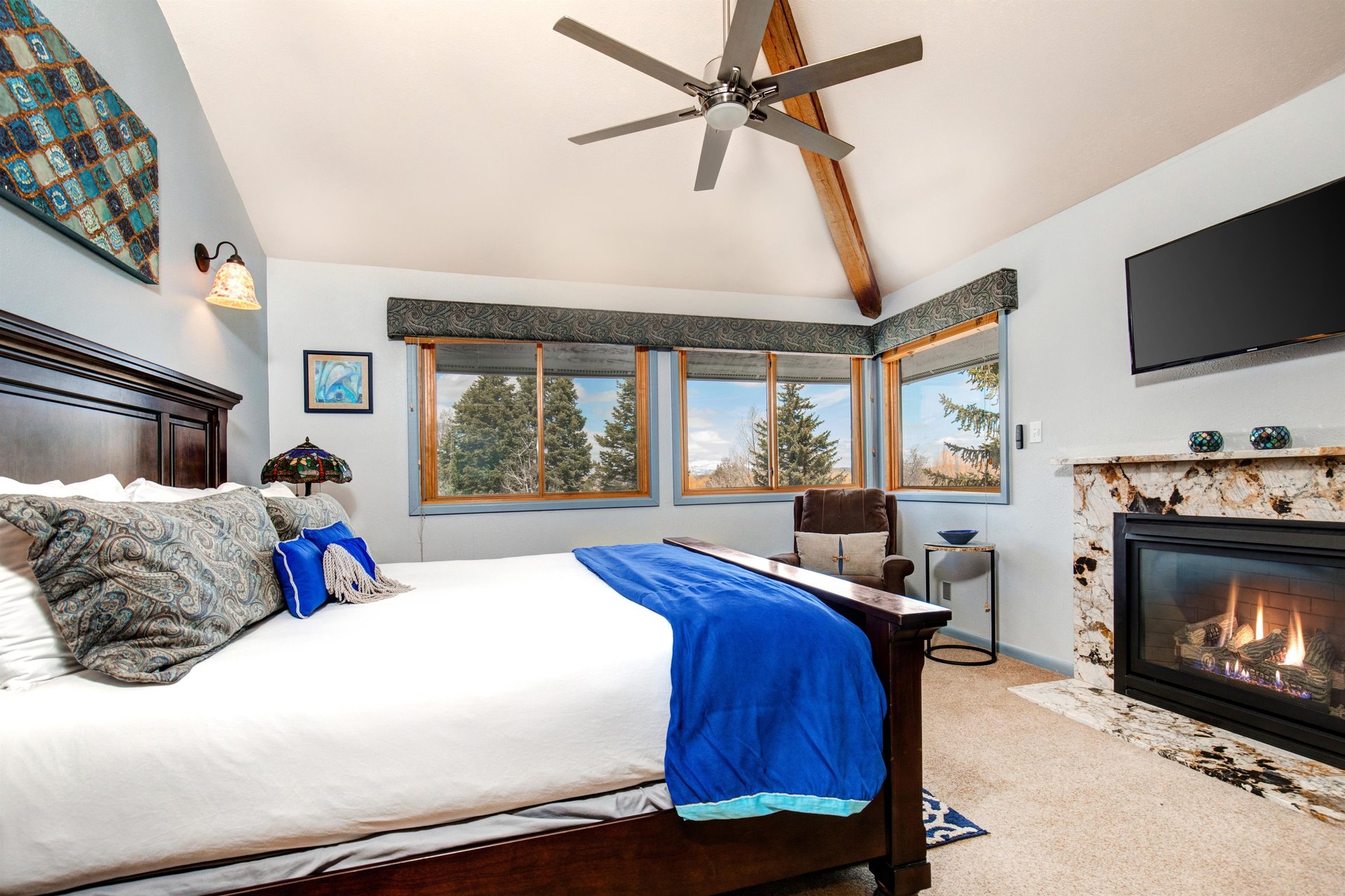 The main suite offers a kingsize bed and large windows framing the evergreen trees.