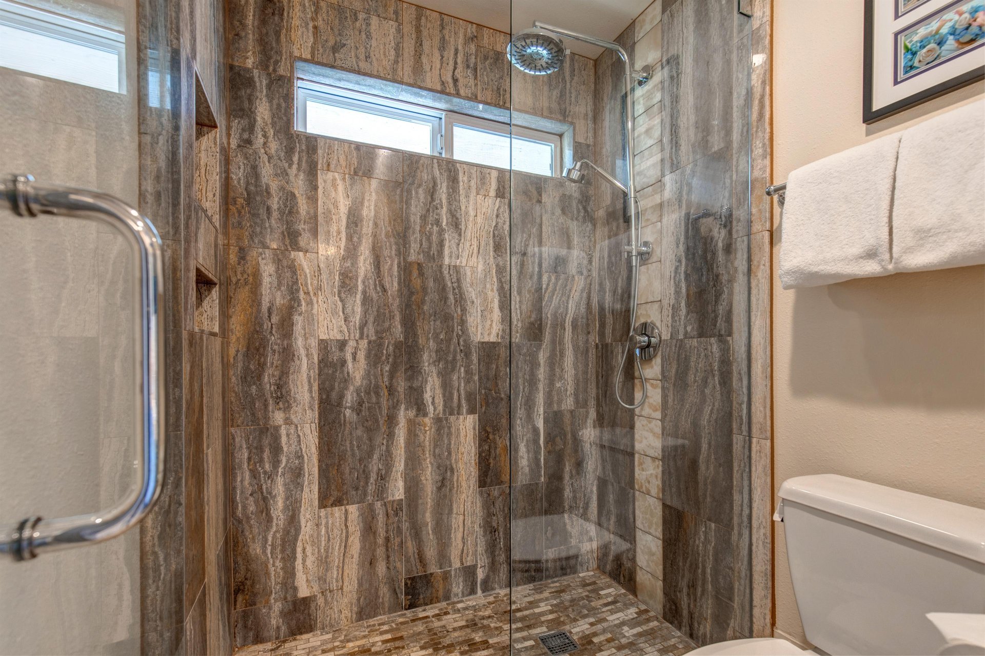 The tiled walkin shower has glass doors.