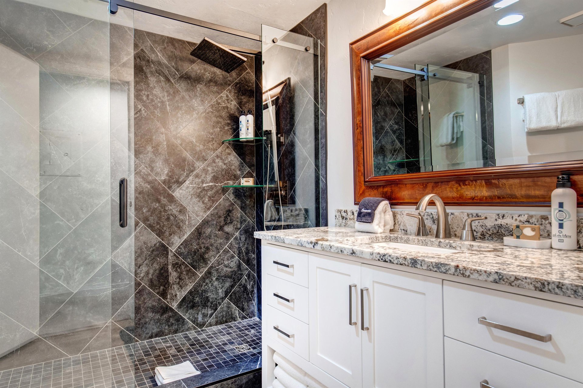 The shared bathroom offers a walkin tiled shower and a single sink white vanity with granite counter.