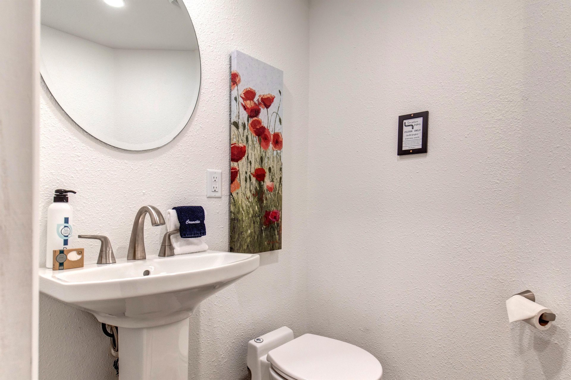 The half bathroom offers a pedestal sink and round mirror.