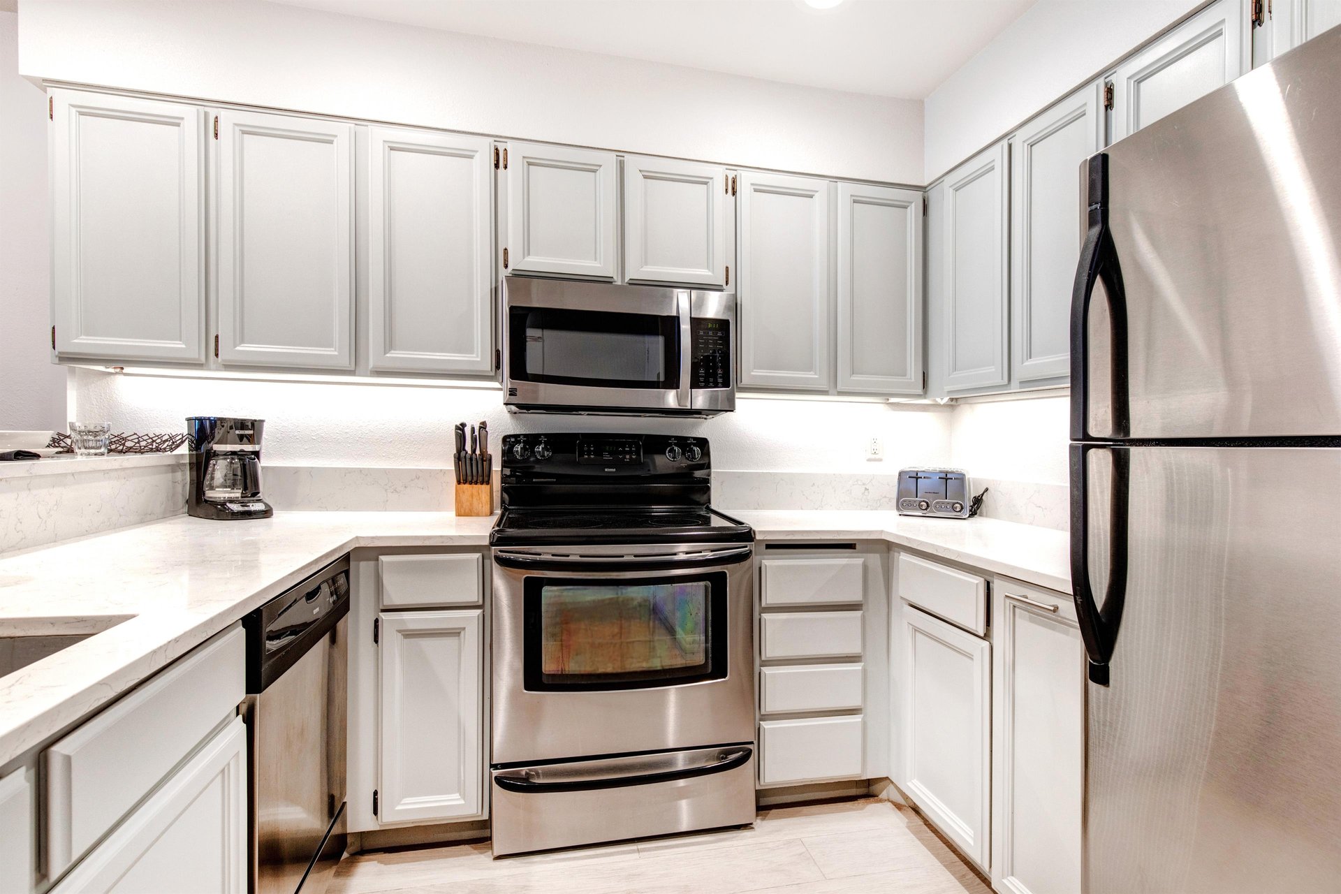 The wellequipped kitchen with light grey cabinets, quartz counters, and stainless steel appliances.
