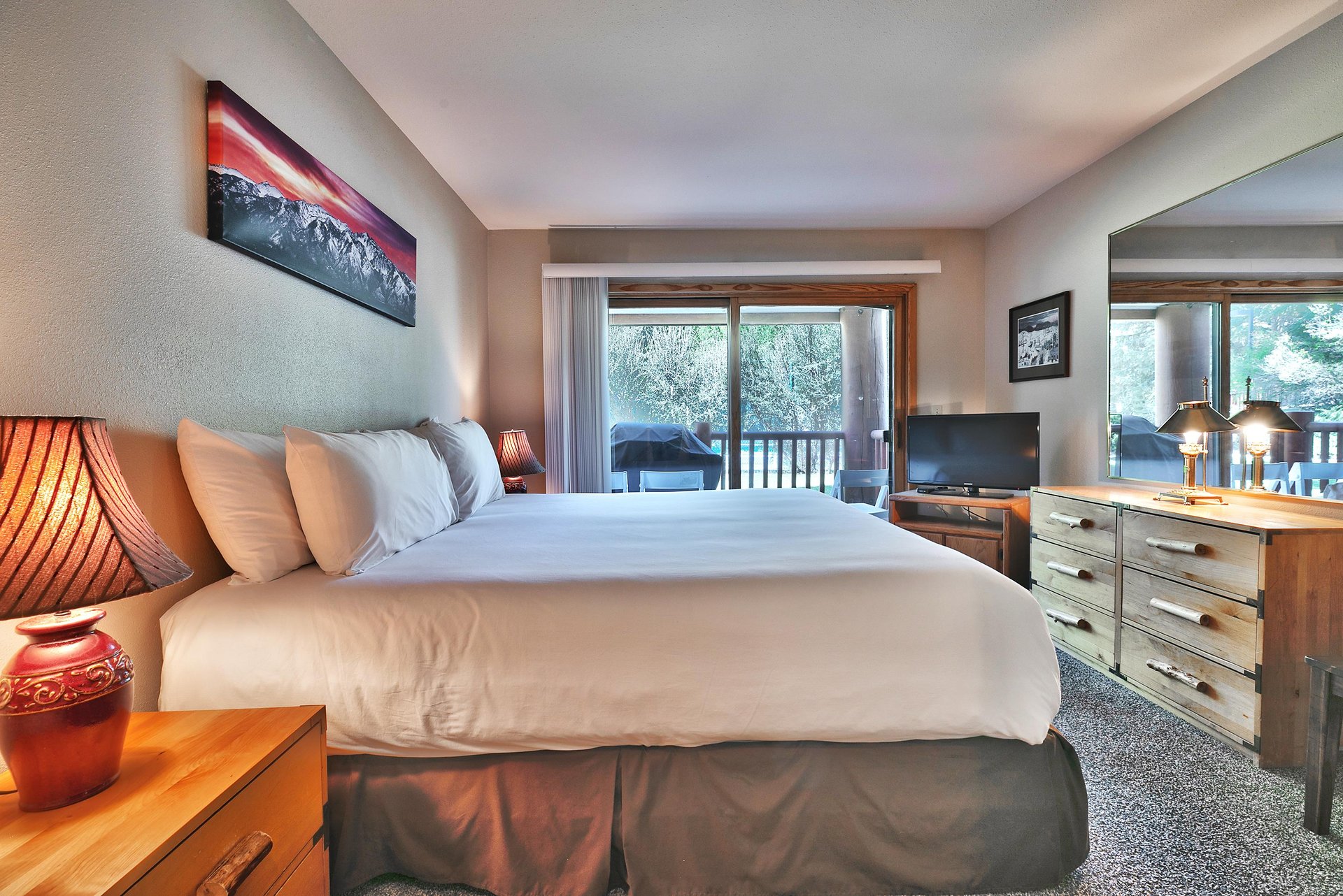 Main bedroom with a king bed covered in white linens, white walls, and large sliding glass doors adding lots of natural light.