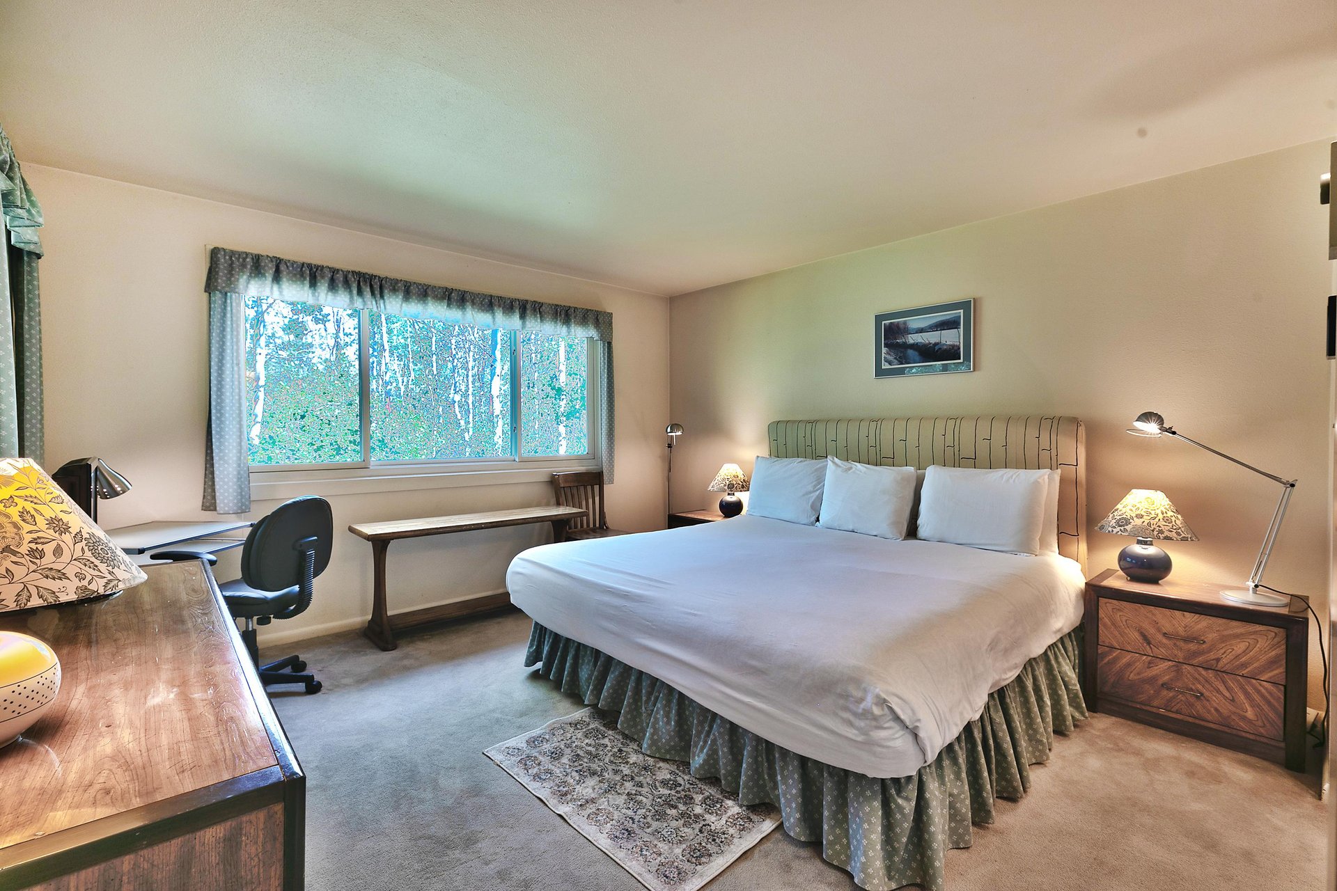 Main bedroom with luxurious king bed with white linens and duvet, work desk, and windows overlooking aspen groves