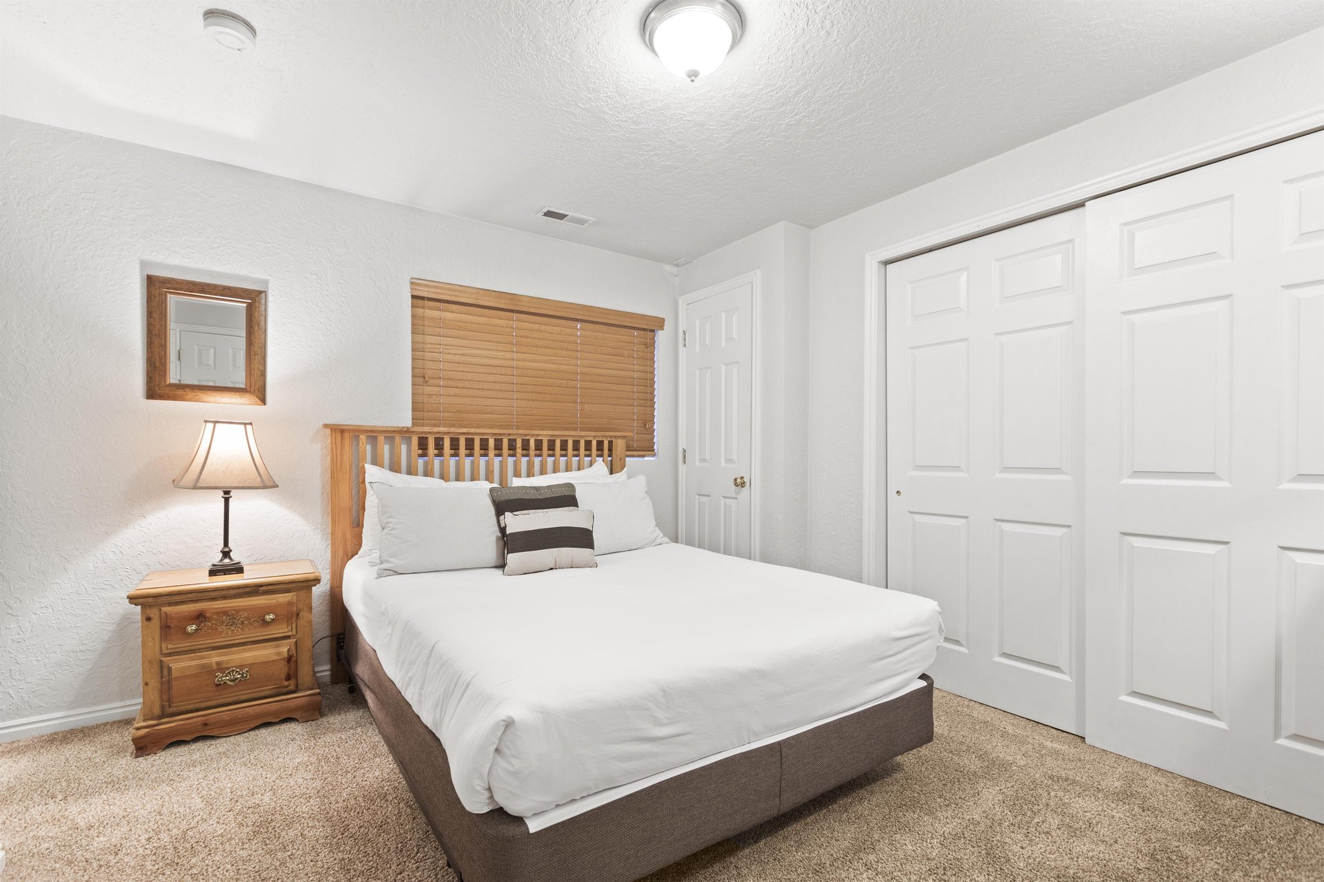 A bedroom with a queen size bed, wooden dresser and white walls and doors.