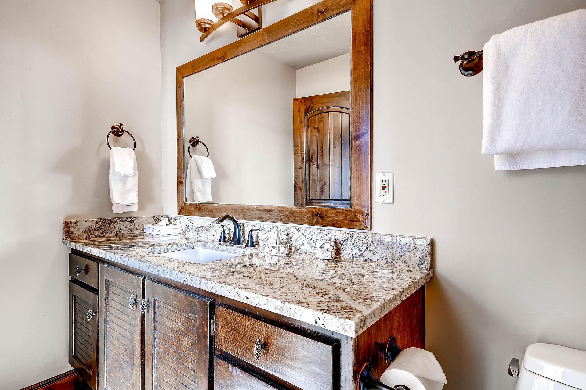 The guest bathroom has a one sink vanity with granite counter and wood cabinet, and large mirror.