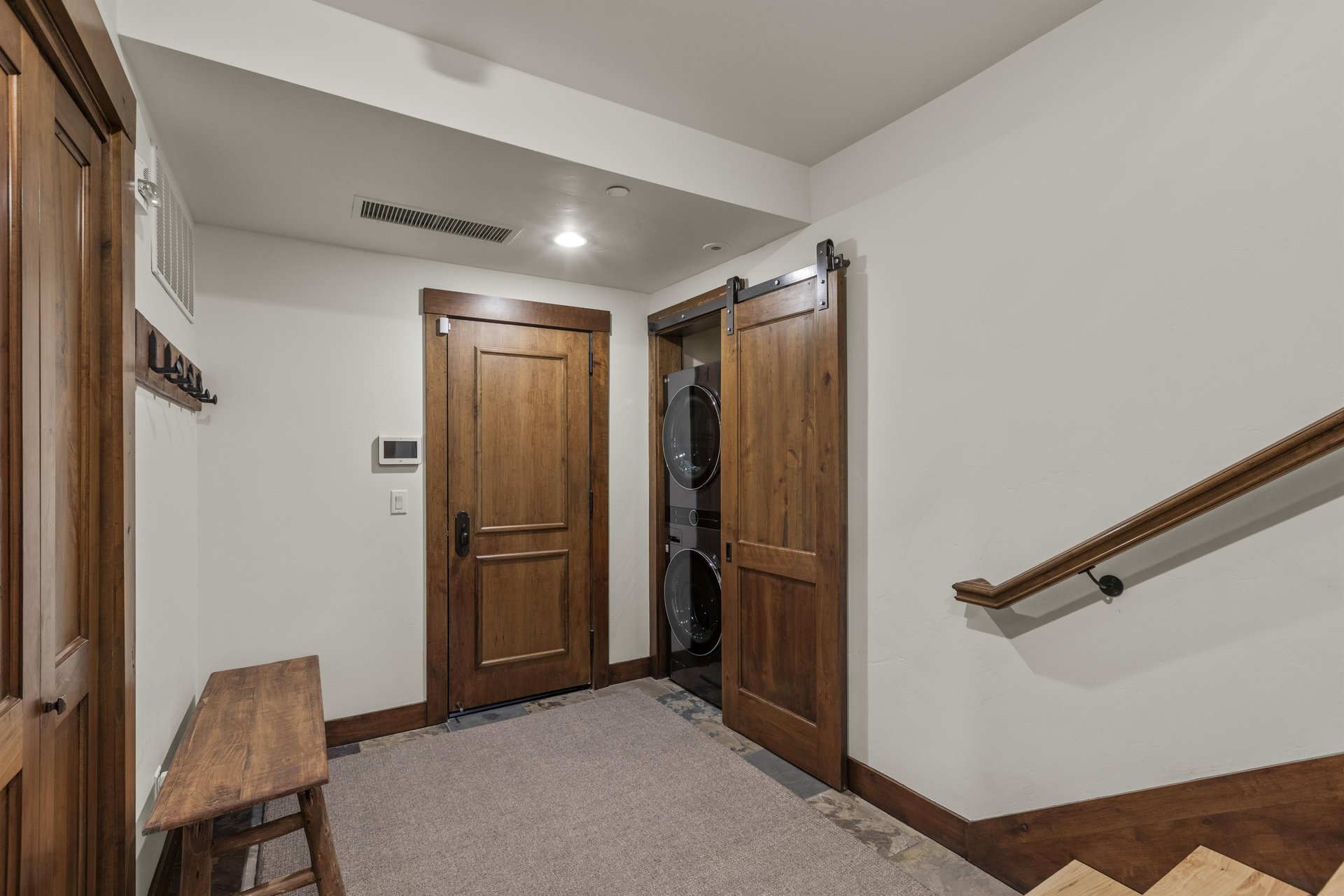 The spacious entry way has a bench to remove shoes and a stacked washer and dryer behind a barn door.