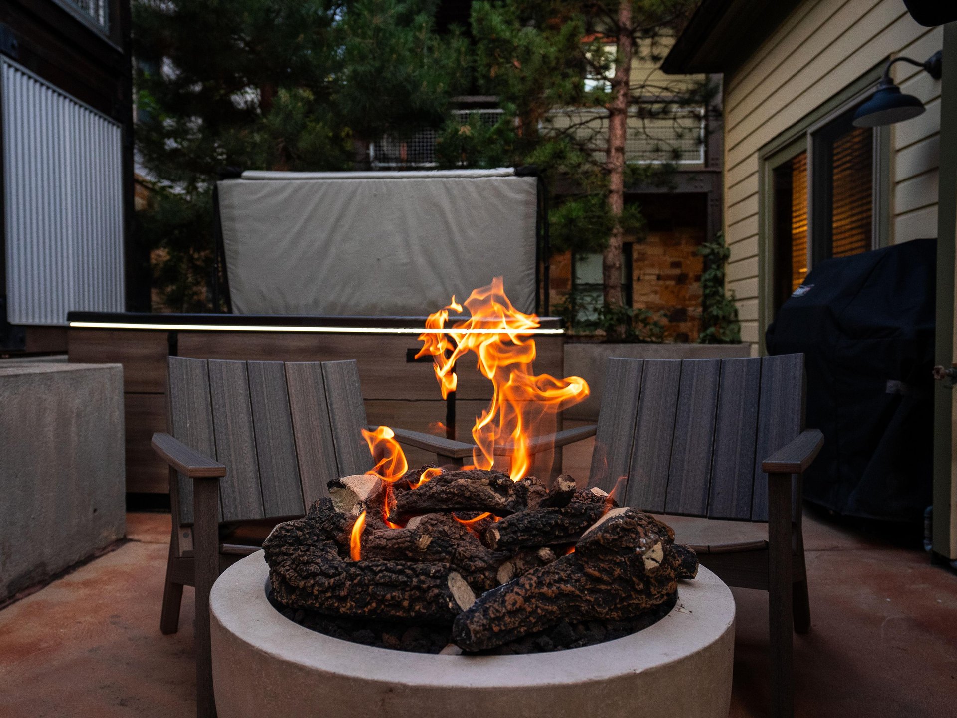 The fire is burning in the gas firepit with two cozy chairs behind it.