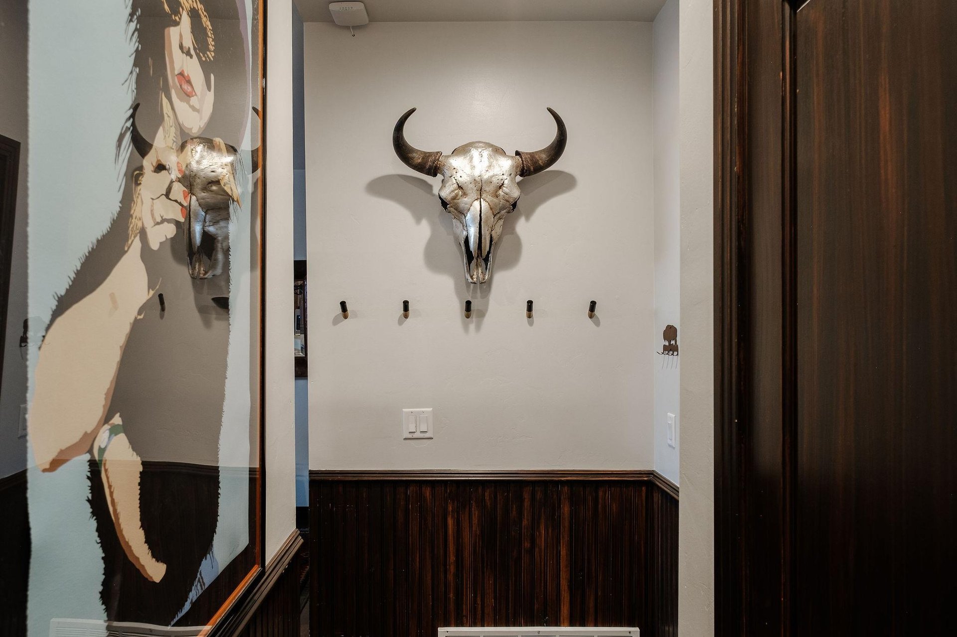 The entryway with hooks for coats, cow head with horns, and stylish art.