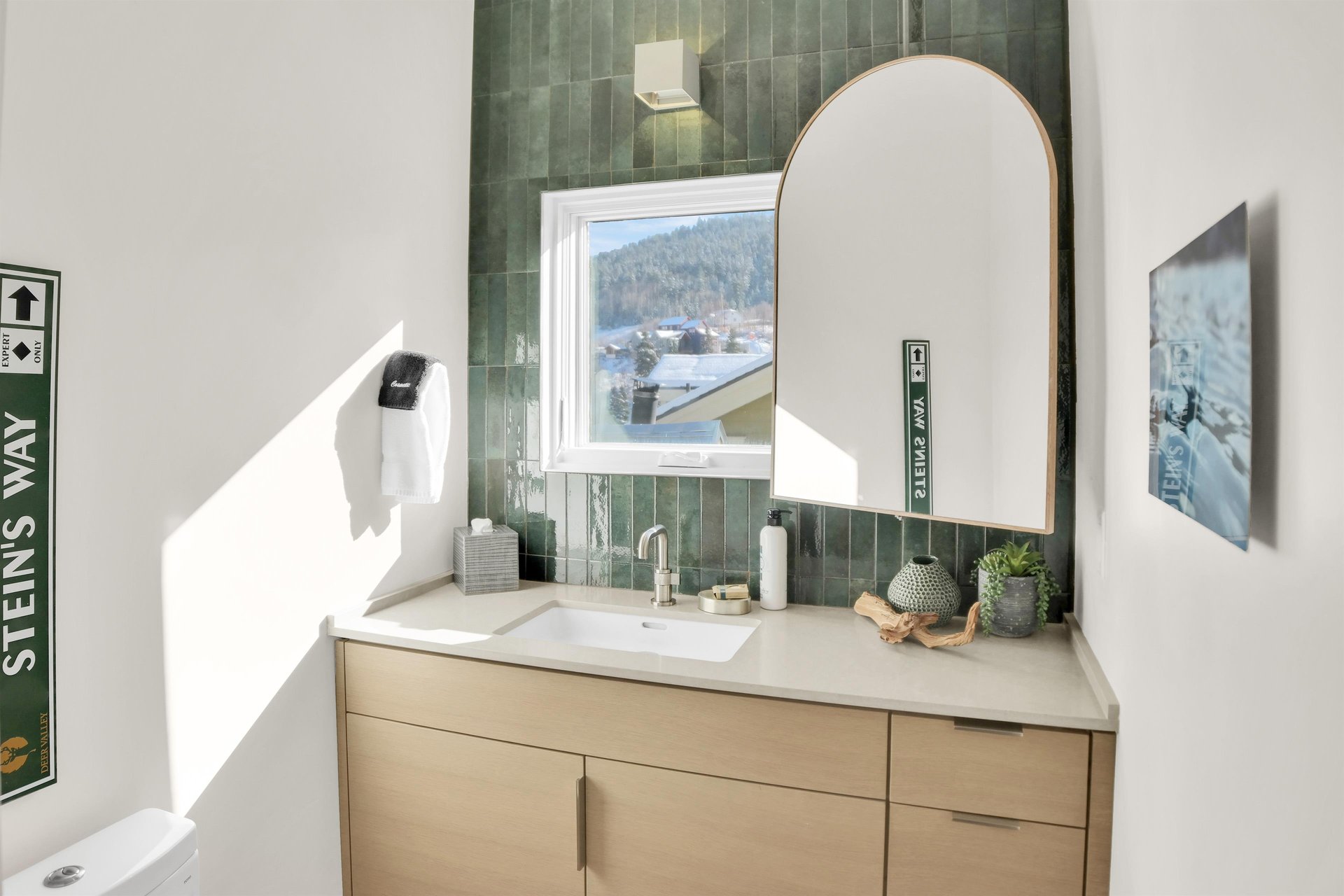 The bathroom has a wood vanity with deep green tile backsplash, window overlooking the mountain and town, and large mirror.