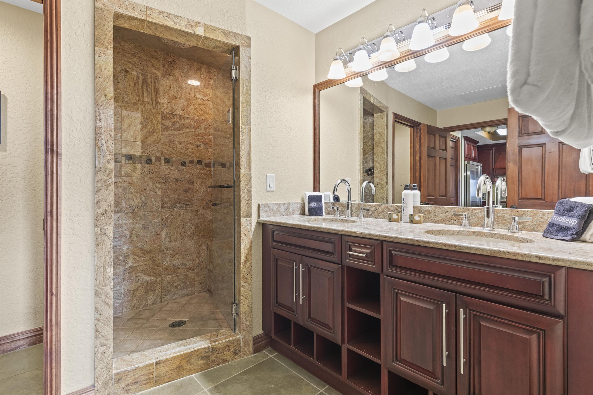Luxurious master bathroom featuring elegant granite surfaces, rich wood cabinetry, and a spacious stonetiled shower.