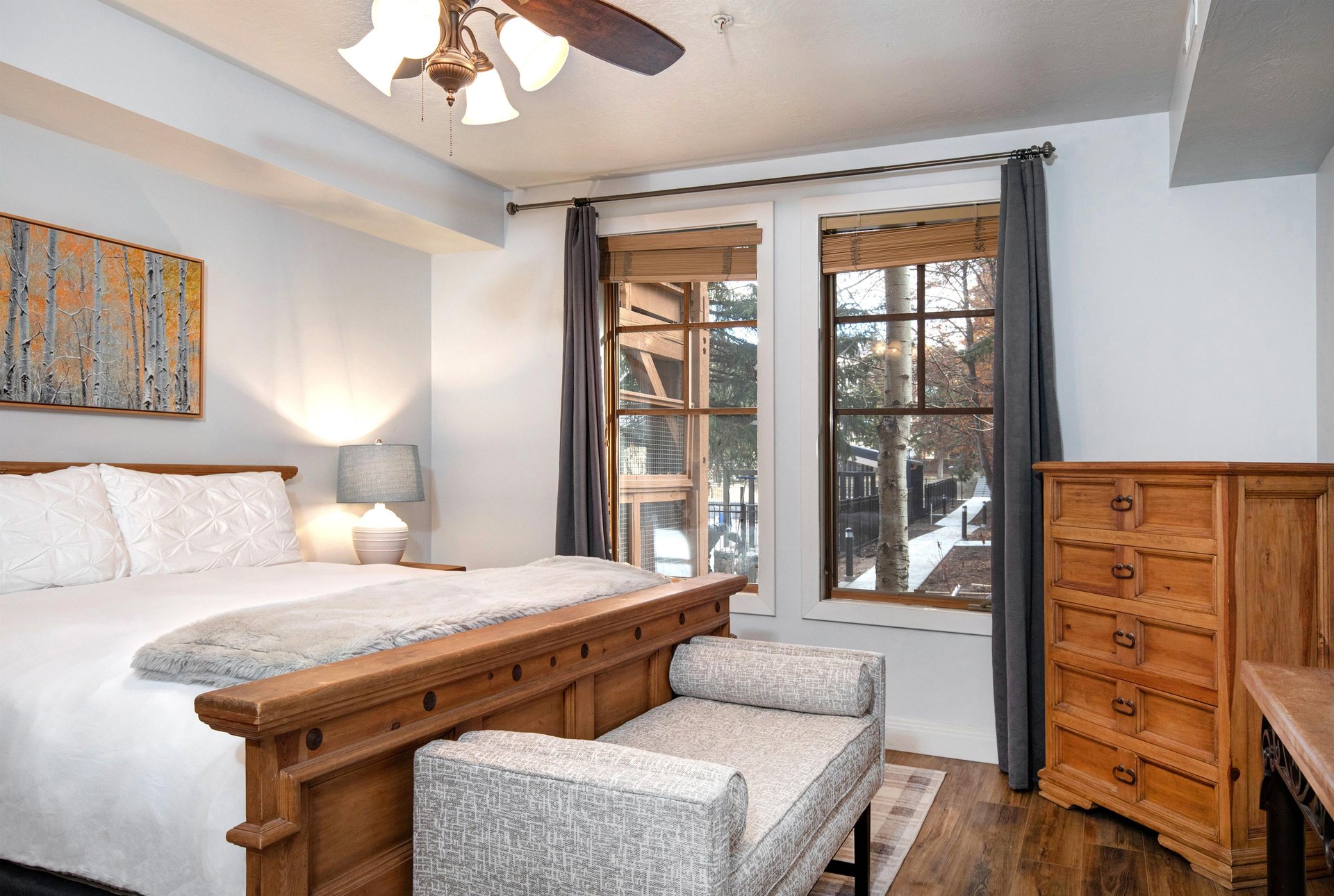 Unwind in your cozy bedroom featuring a comfortable bed, warm wood furnishings, and large windows.