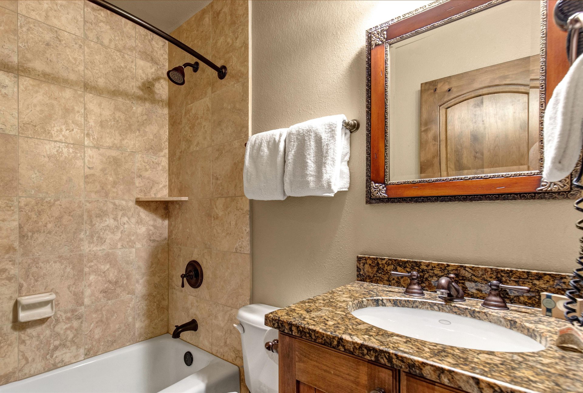 Unwind in your elegant bathroom featuring travertine tiles, granite countertops, and plush towels for your comfort.