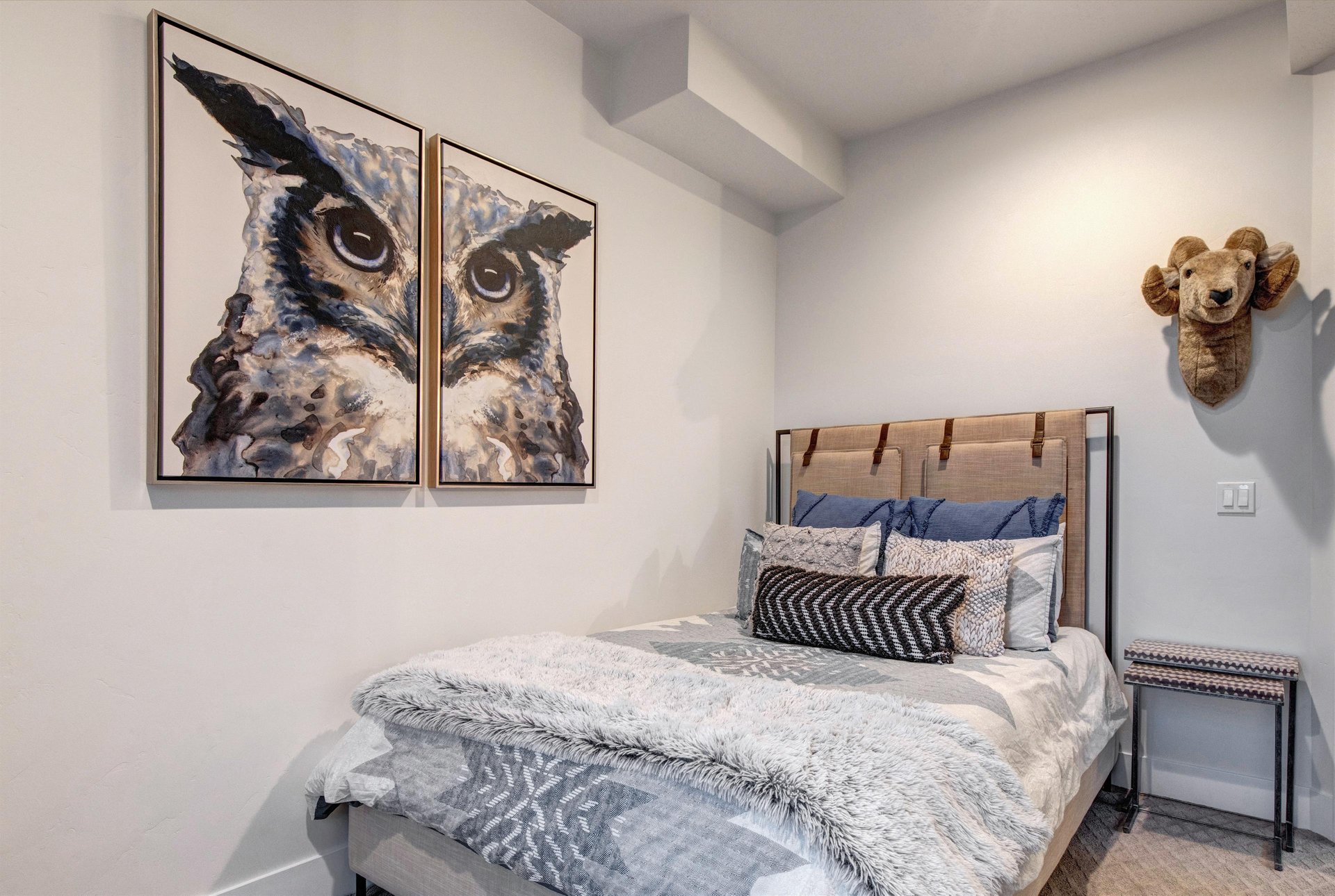 A cozy bedroom with a queensize bed, owl art, and stylish bed frame and linens.