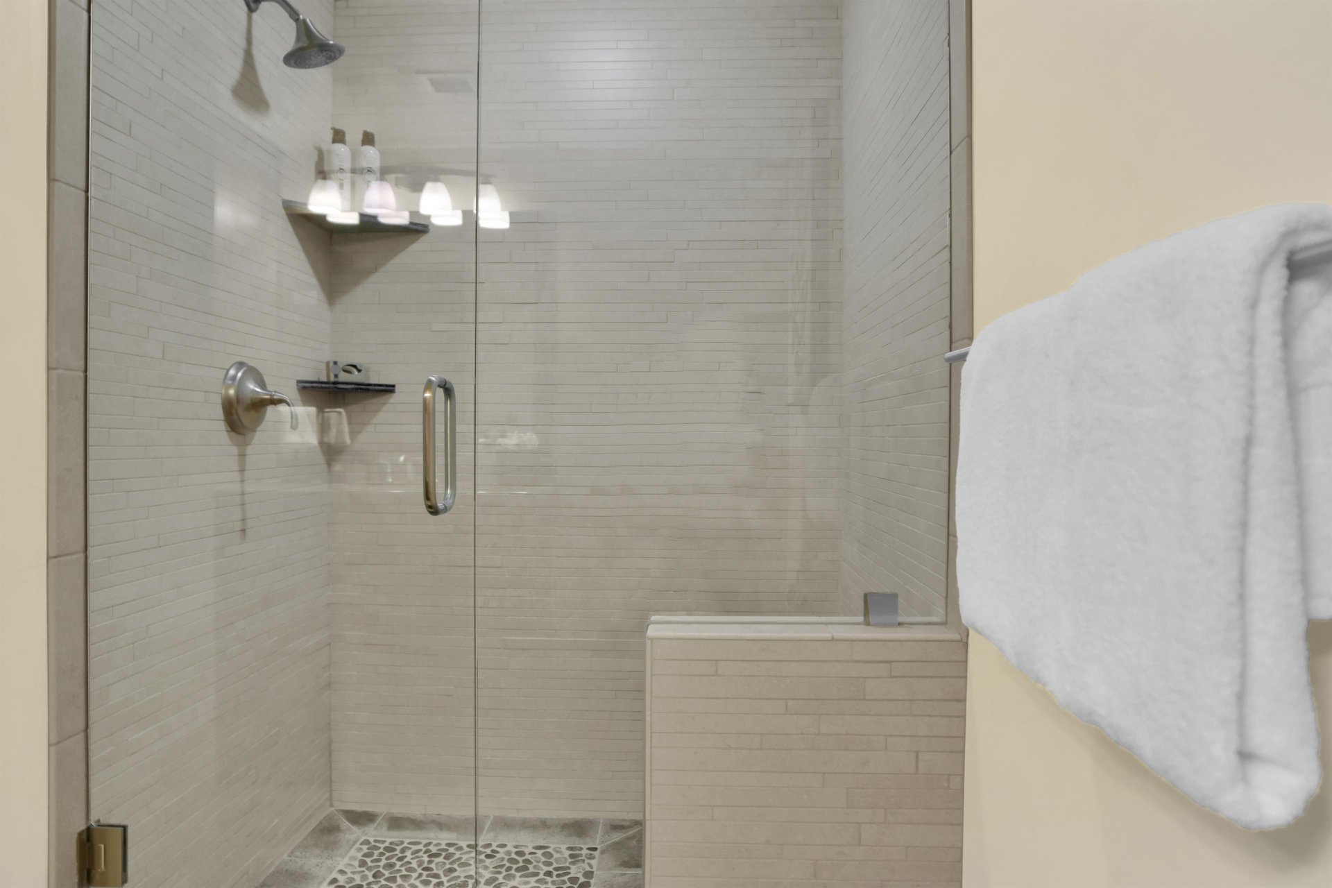 The walk in shower has cream colored tile walls, stone floor and a glass enclosure door.
