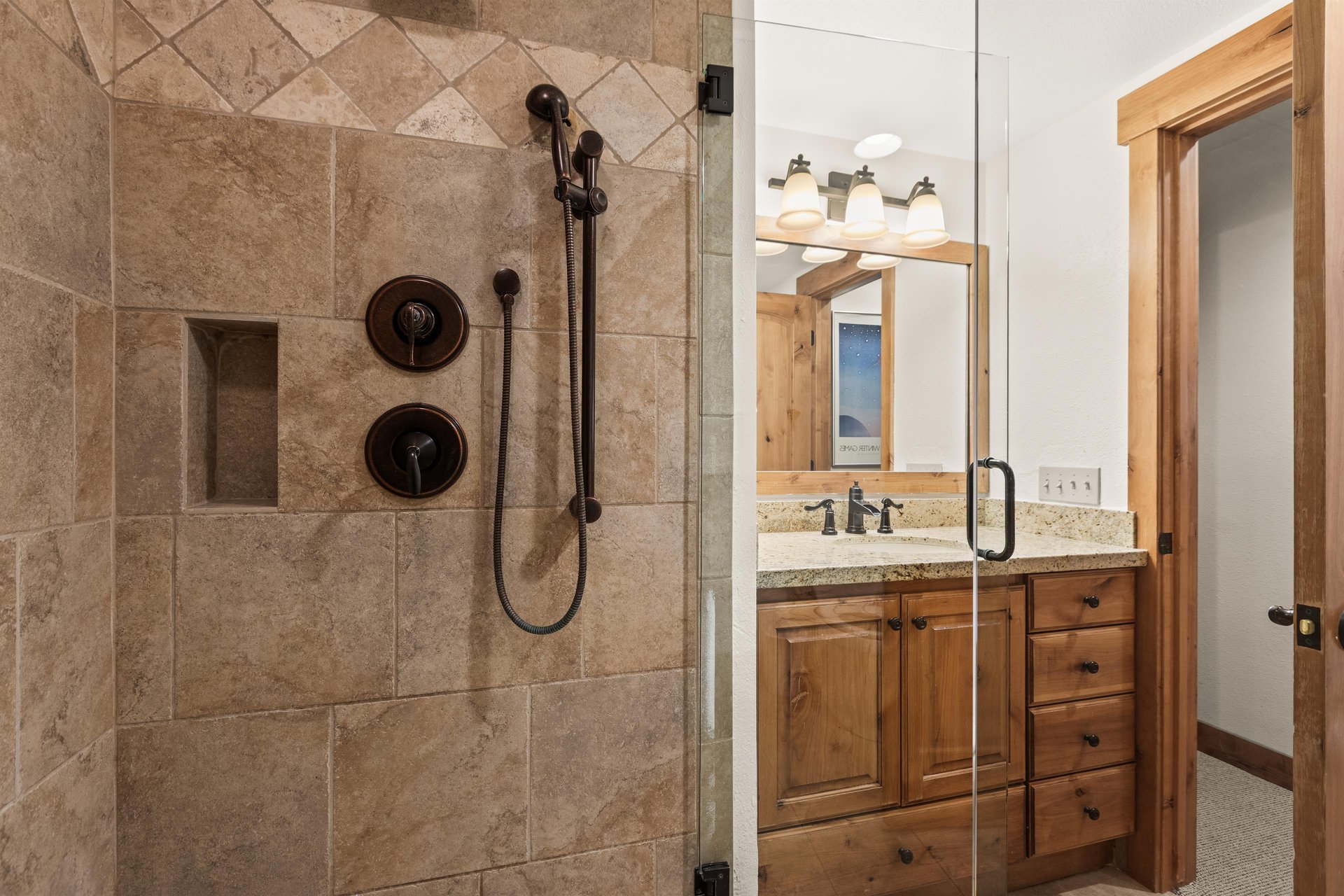 The shared bathroom has a walkin shower with a glass door and beautiful tile.