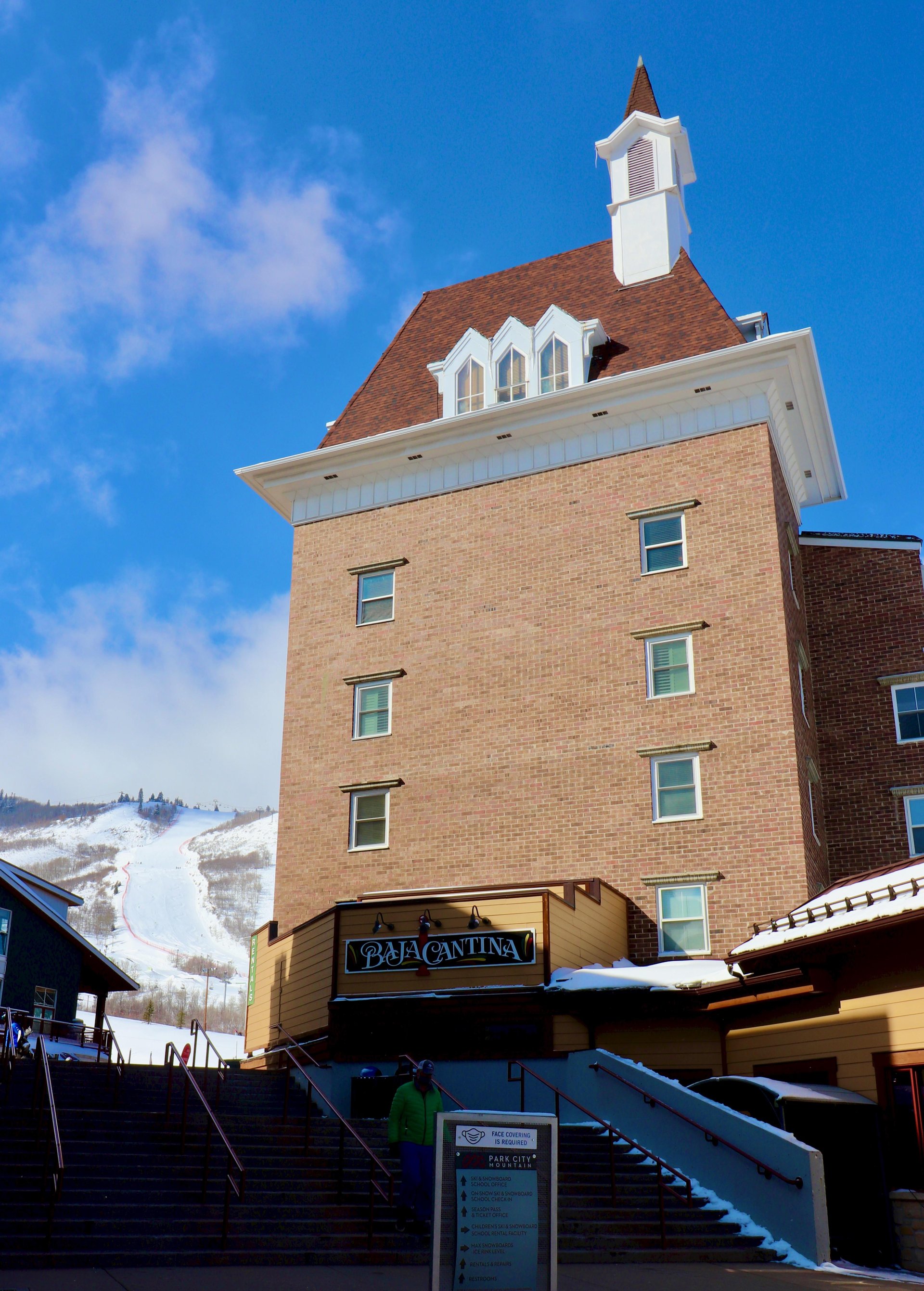 View of Resort Plazas brick façade with snowy ski runs at Park City Mountain next to it.