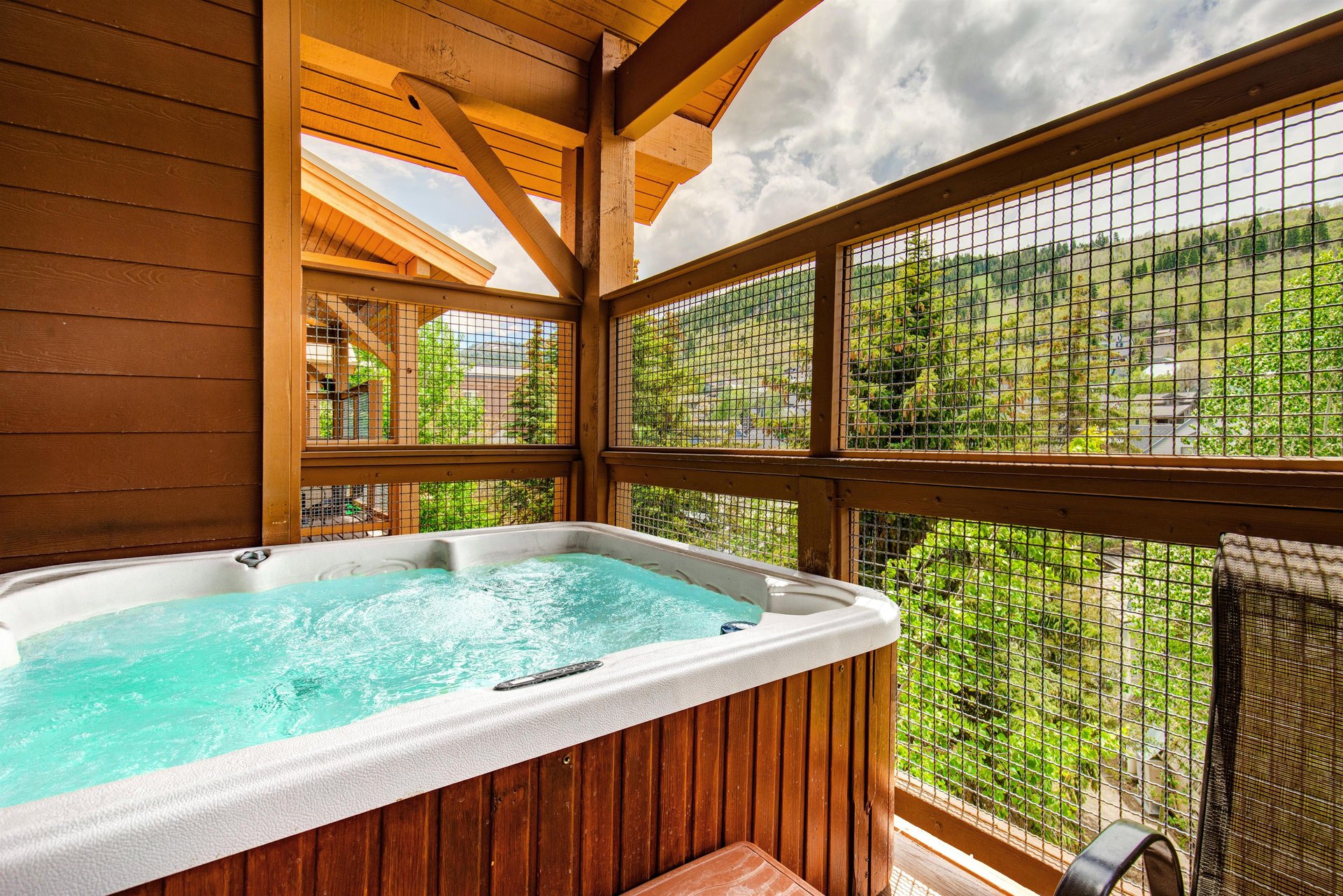 Soak in the bubbling hot tub under vaulted timber ceilings while gazing at mountain views and lush greenery through screened windows—your perfect private retreat for relaxation.