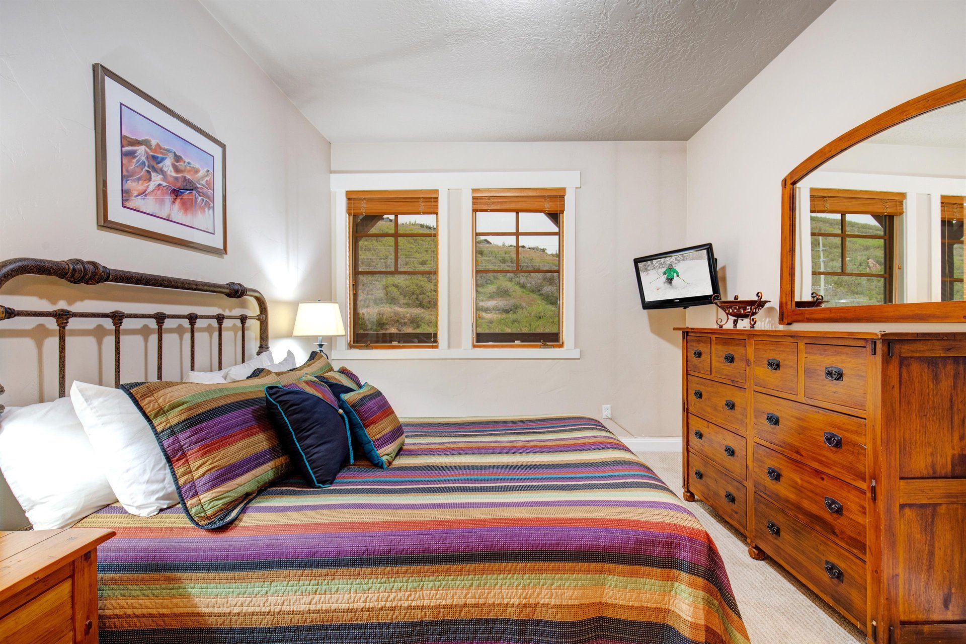 Wake up to peaceful desert views through the windows of this cozy bedroom, complete with a handcrafted wooden bed, vibrant quilted linens, and a charming dresser with mirror.