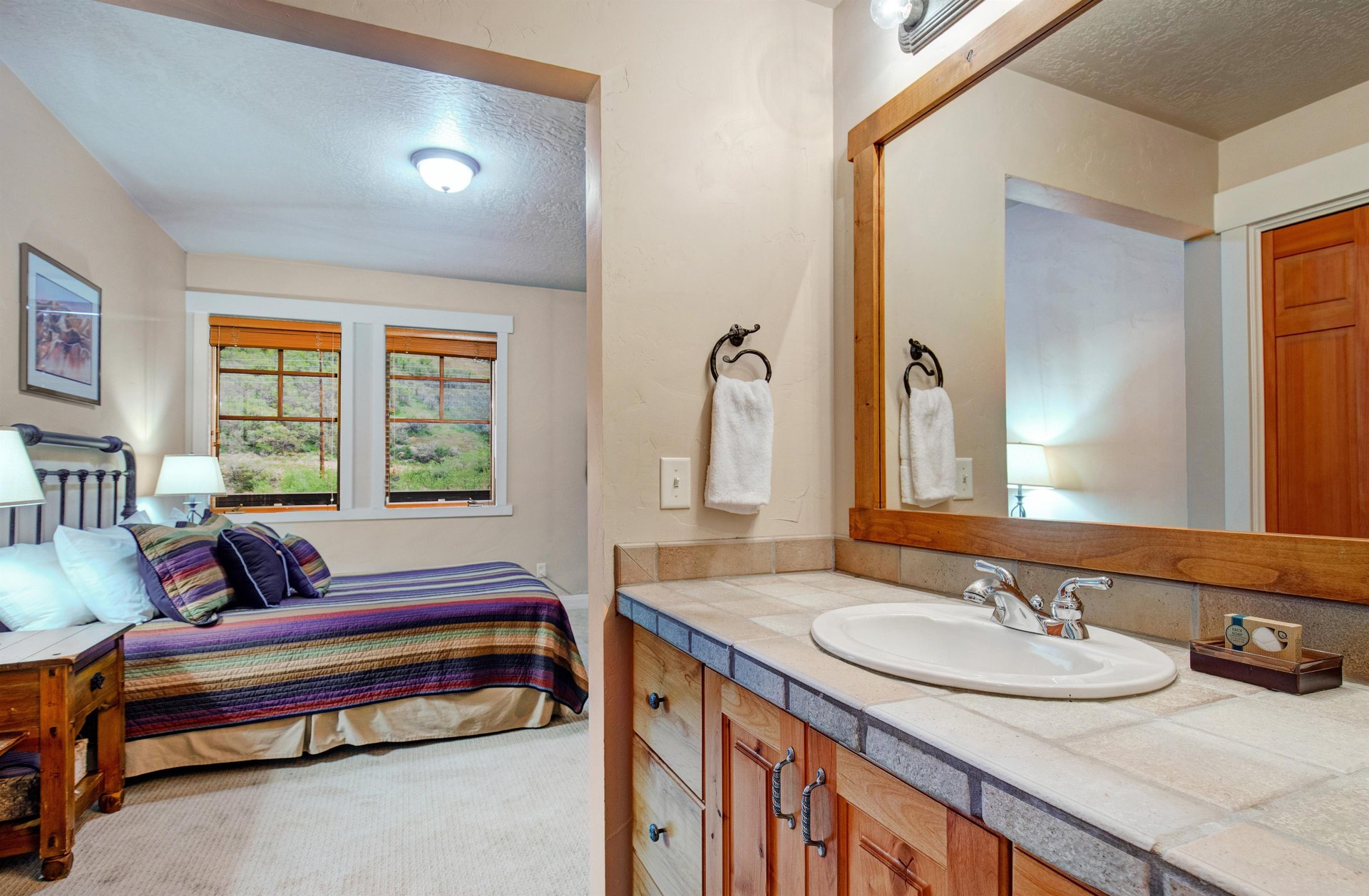 Unwind in your private suite featuring a comfortable bed with vibrant linens, warm wood accents, and an ensuite vanity with fresh towels awaiting your arrival.