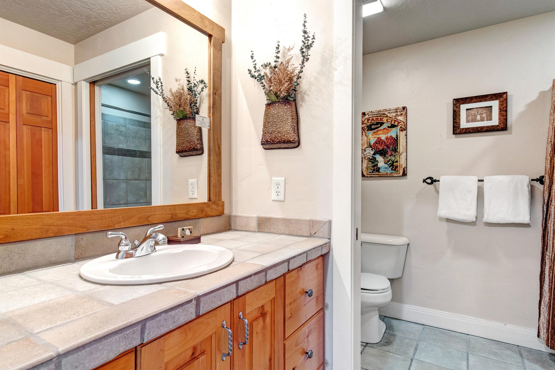 Step into your private bathroom featuring warm wood cabinetry, a tiled vanity, and a separate shower area stocked with fresh towels for your comfort.