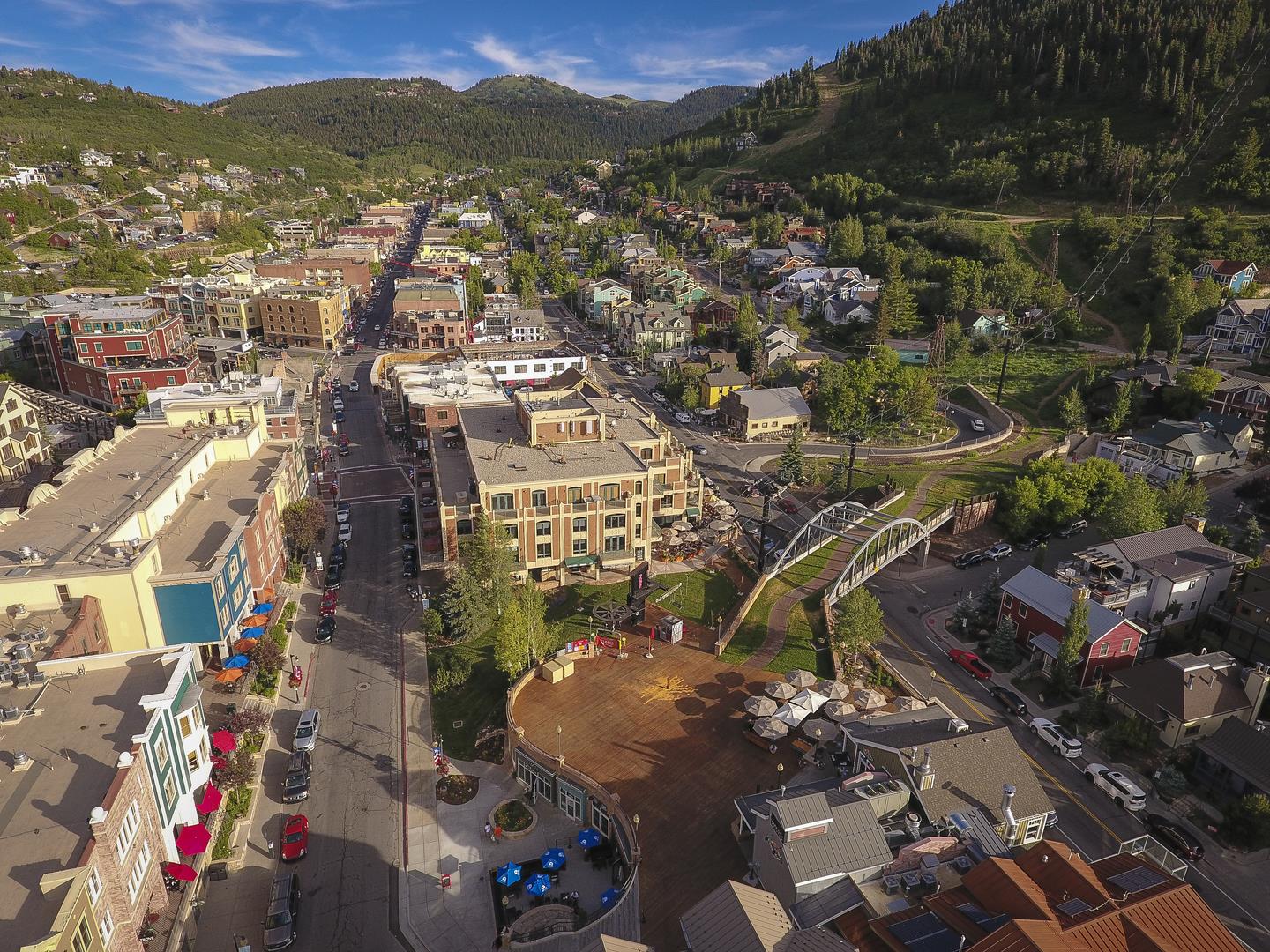 Aerial view of a charming mountain town nestled in a scenic valley, with forested peaks rising beyond the historic downtown core and surrounding residential neighborhoods.