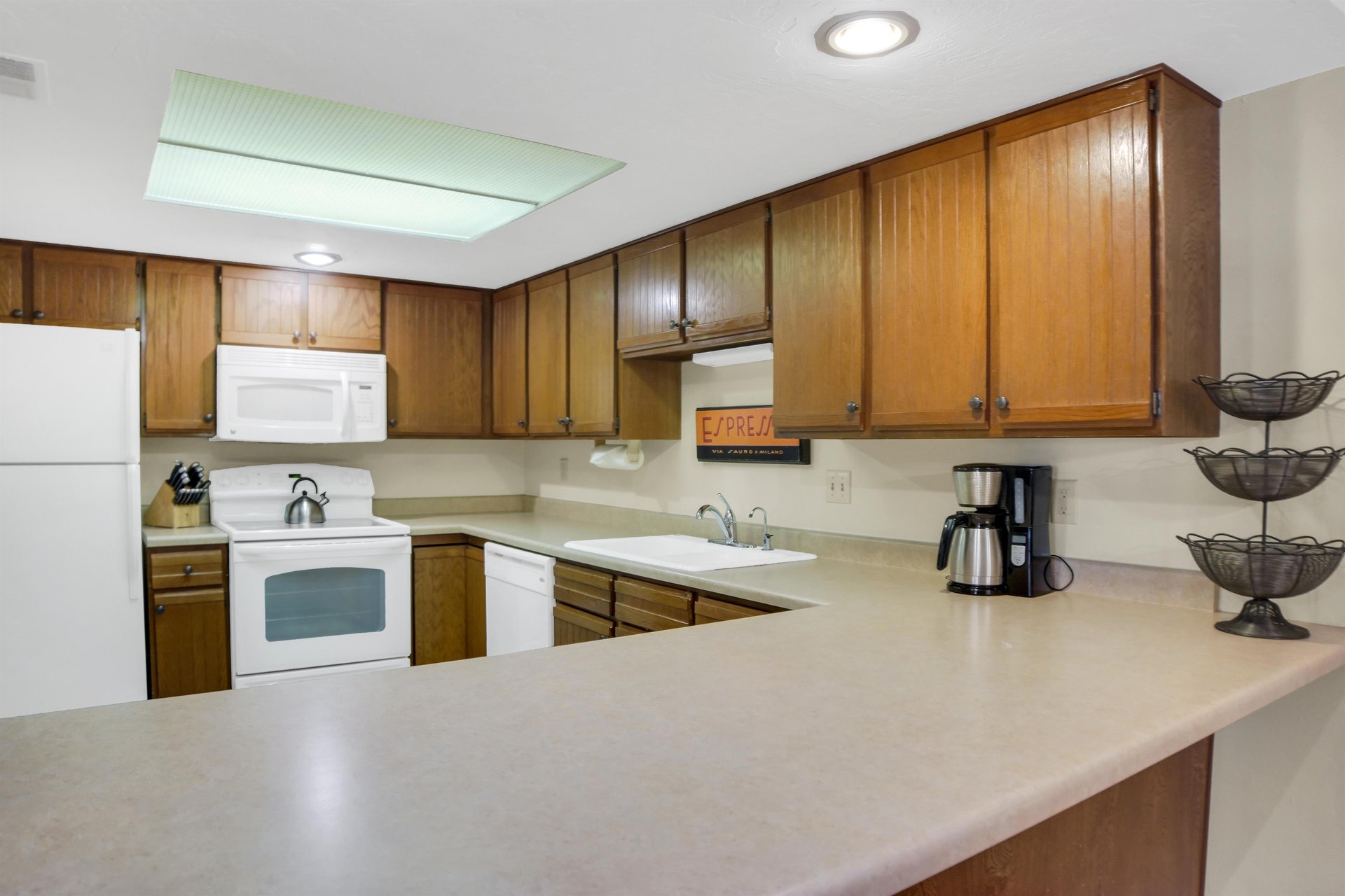 Park Station 122s kitchen has wood cabinets, white appliances, cream counters, white walls, and grey tiled floors.