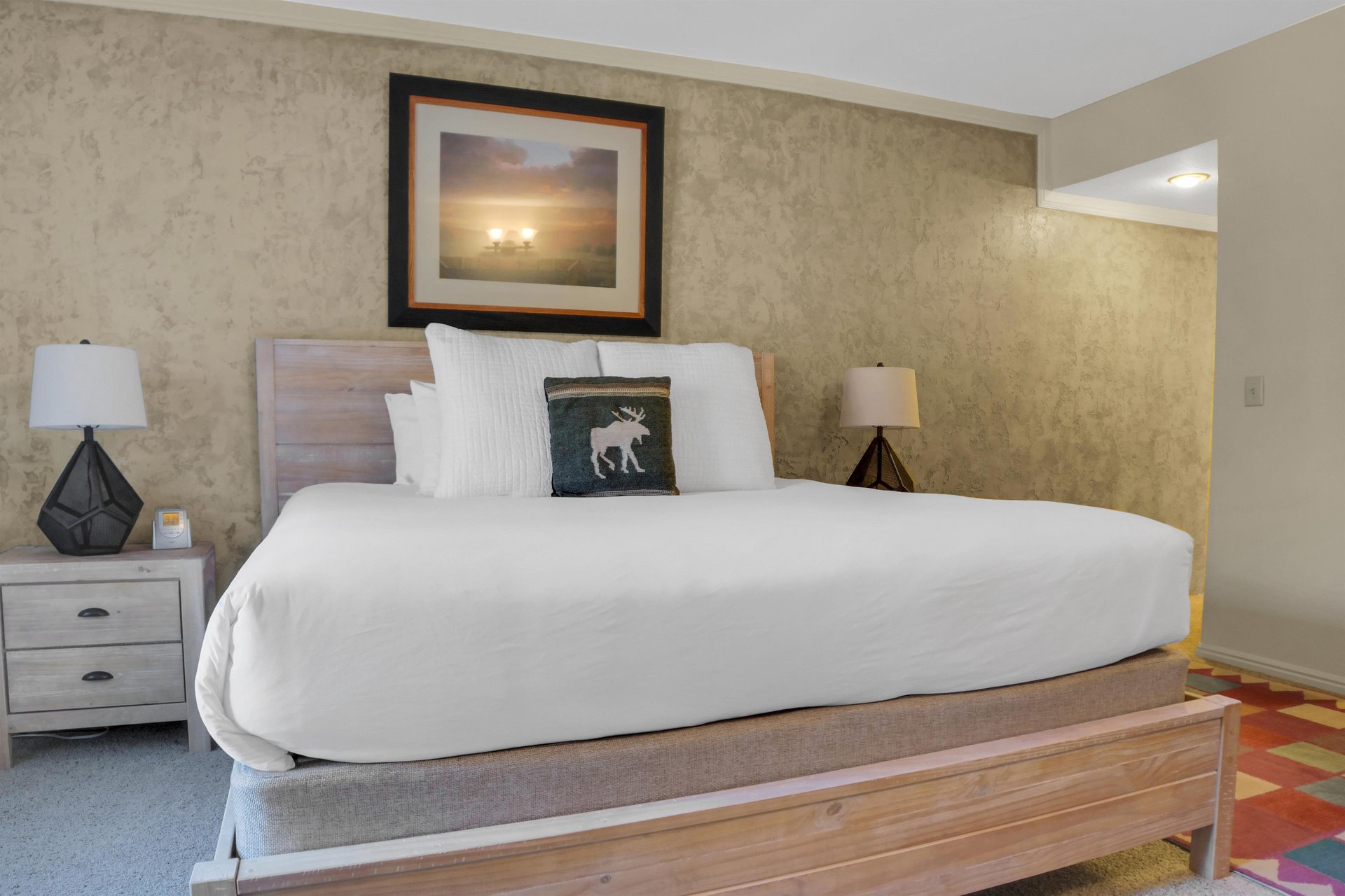 Park Station 122s main suite king bed with a wood frame and headboard, 2 nightstands and lamps, and large picture above.