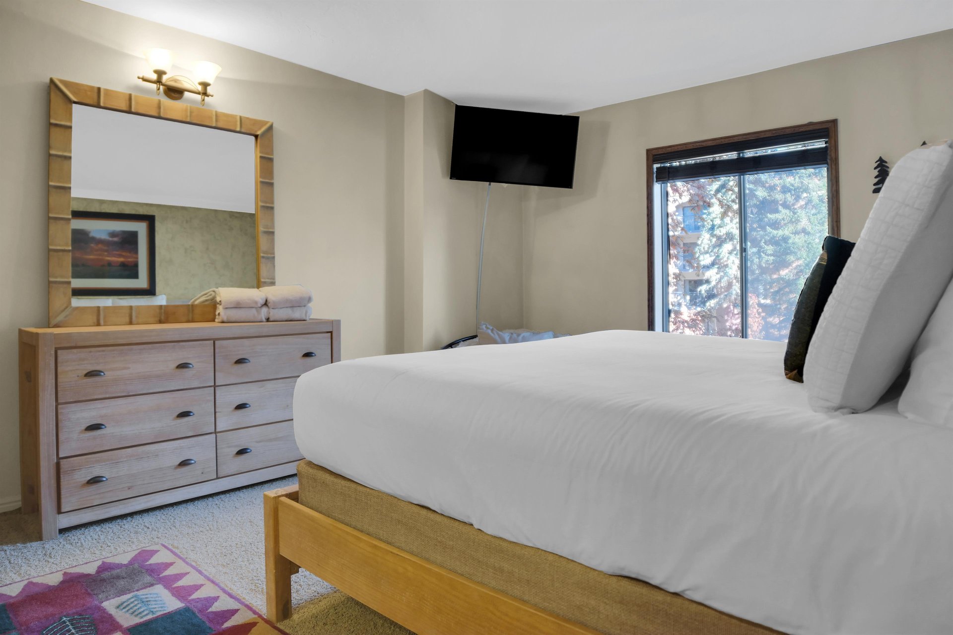 Park Station 122s main suite king bed, wood dresser, large mirror, TV, and large window.