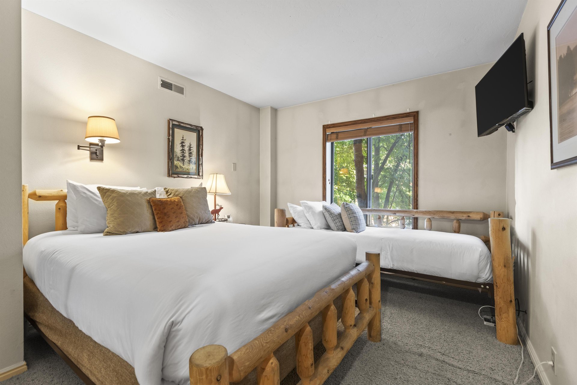 The second bedroom with a queen bed, and a twin bed next to a window with a view of the trees.