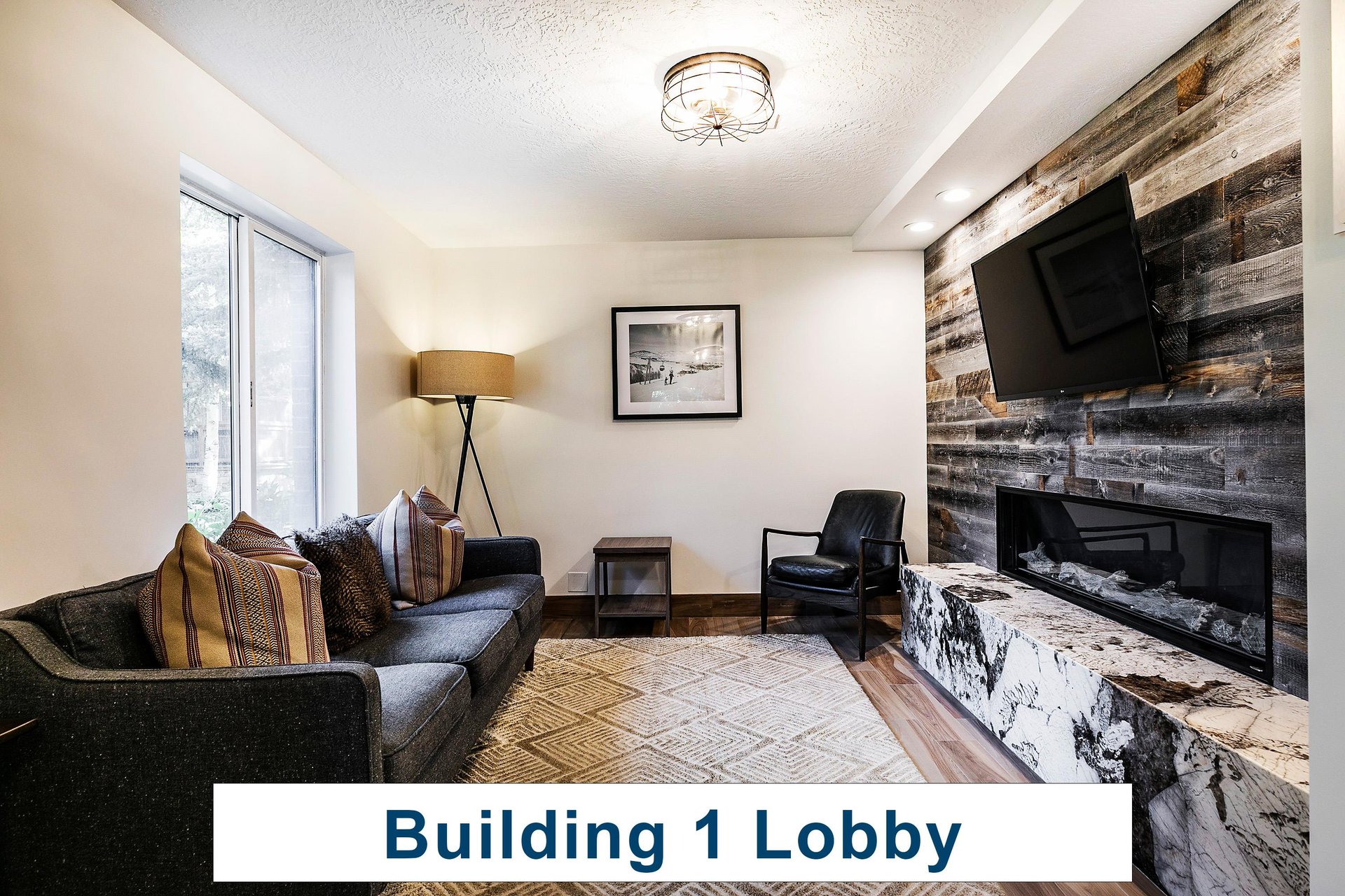 Building 1 lobby entrance with large area rug, dark gray sofa, fireplace, TV, and black leather accent chair.