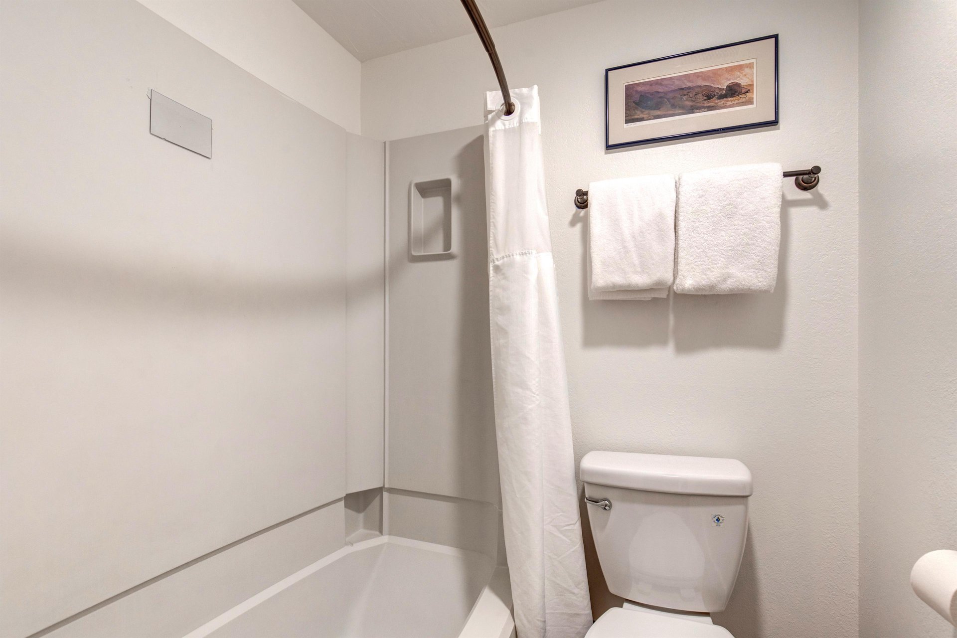 The shared bathroom has a white shower and bathtub surround with a white shower curtain and a white toilet.