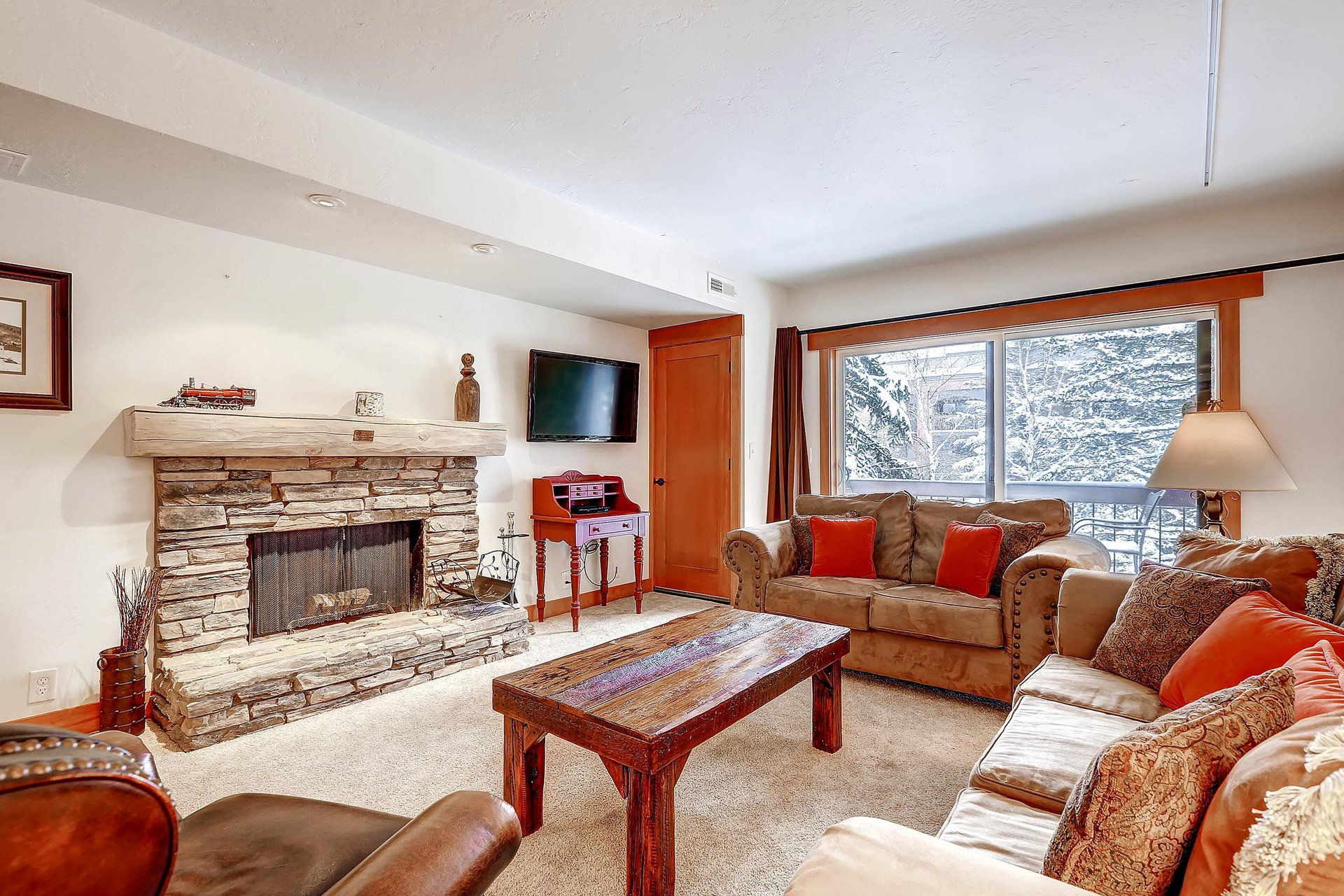 Park Station 134s living room with griege upholstered couch, red throw pillows, large sliding glass doors, and fireplace.