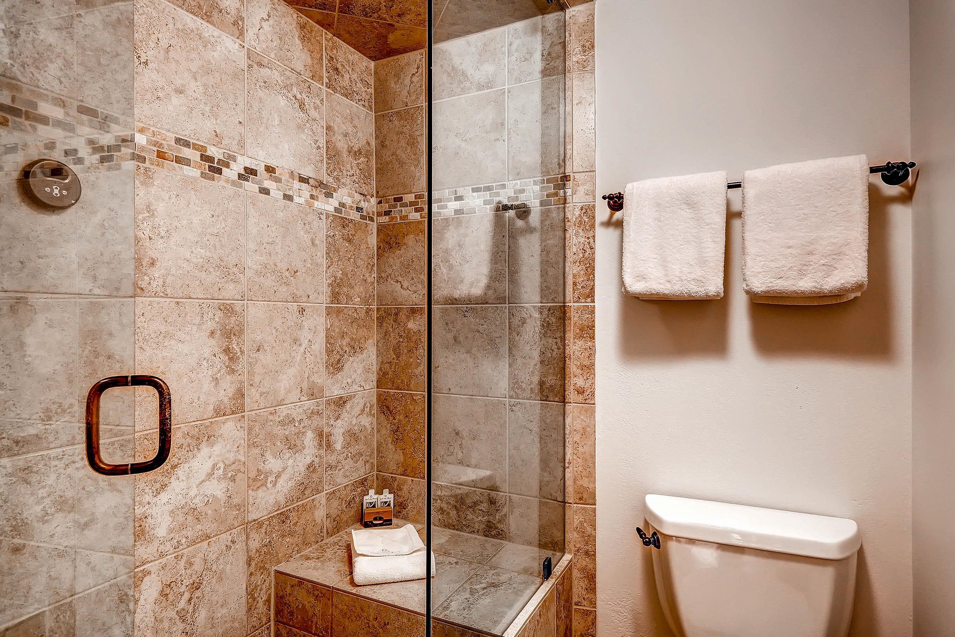 Park Station 134s main bathroom with a cream colored tiled shower with glass panel and white toilet next to it.