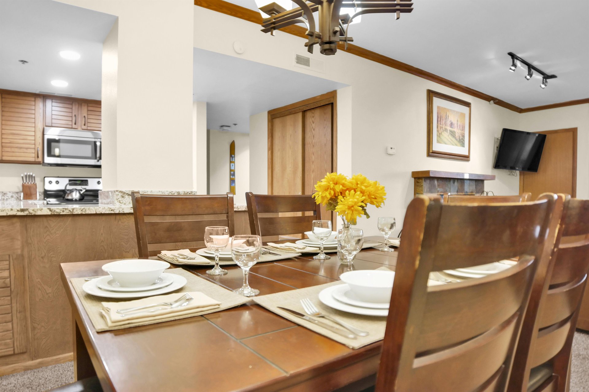 Park Station 214s dining table is set for 6 guests with white dishes, cream placemats and yellow flowers in the center.