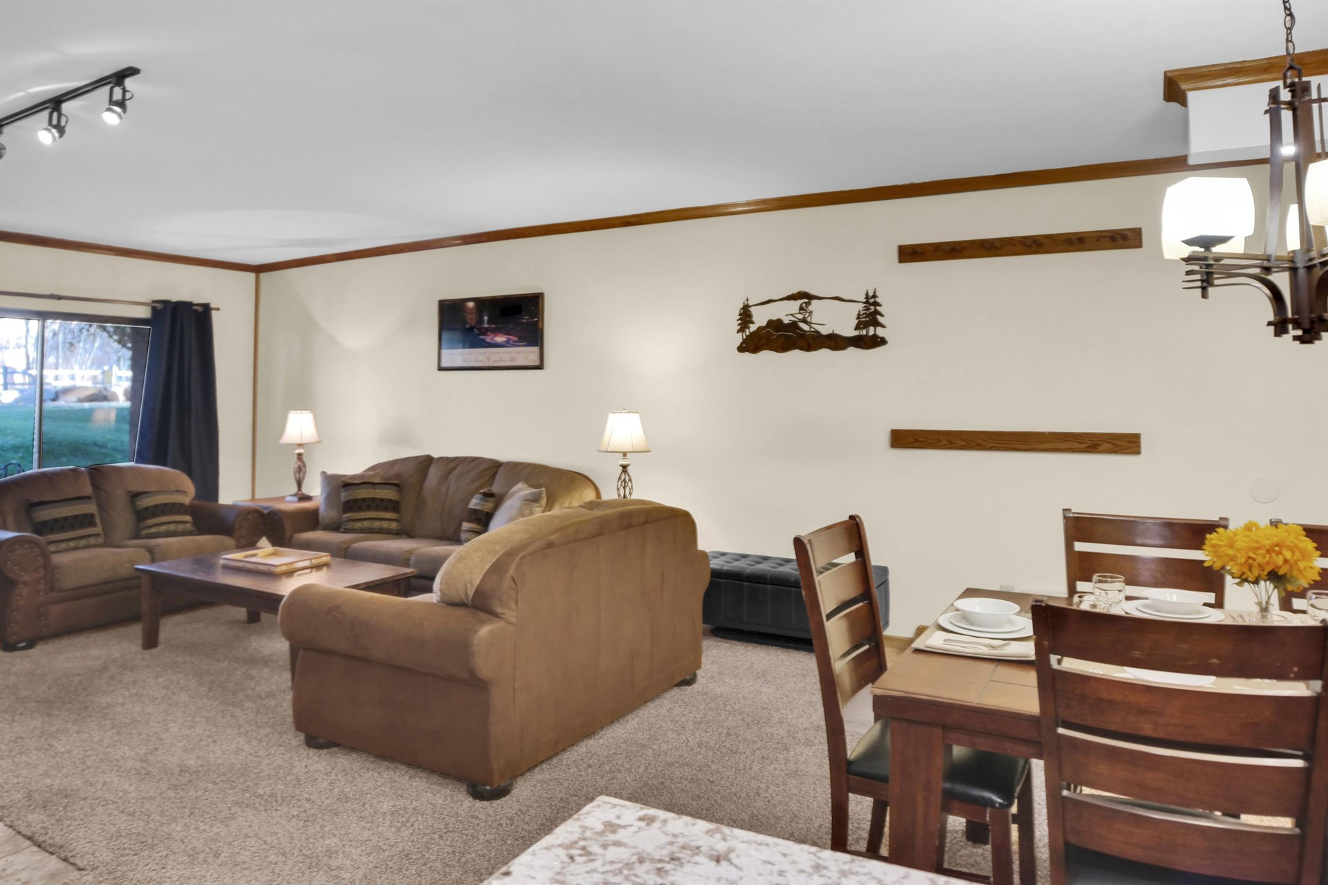 The dining area and living room area with a leather storage ottoman and ski racks on the wall by the entry.