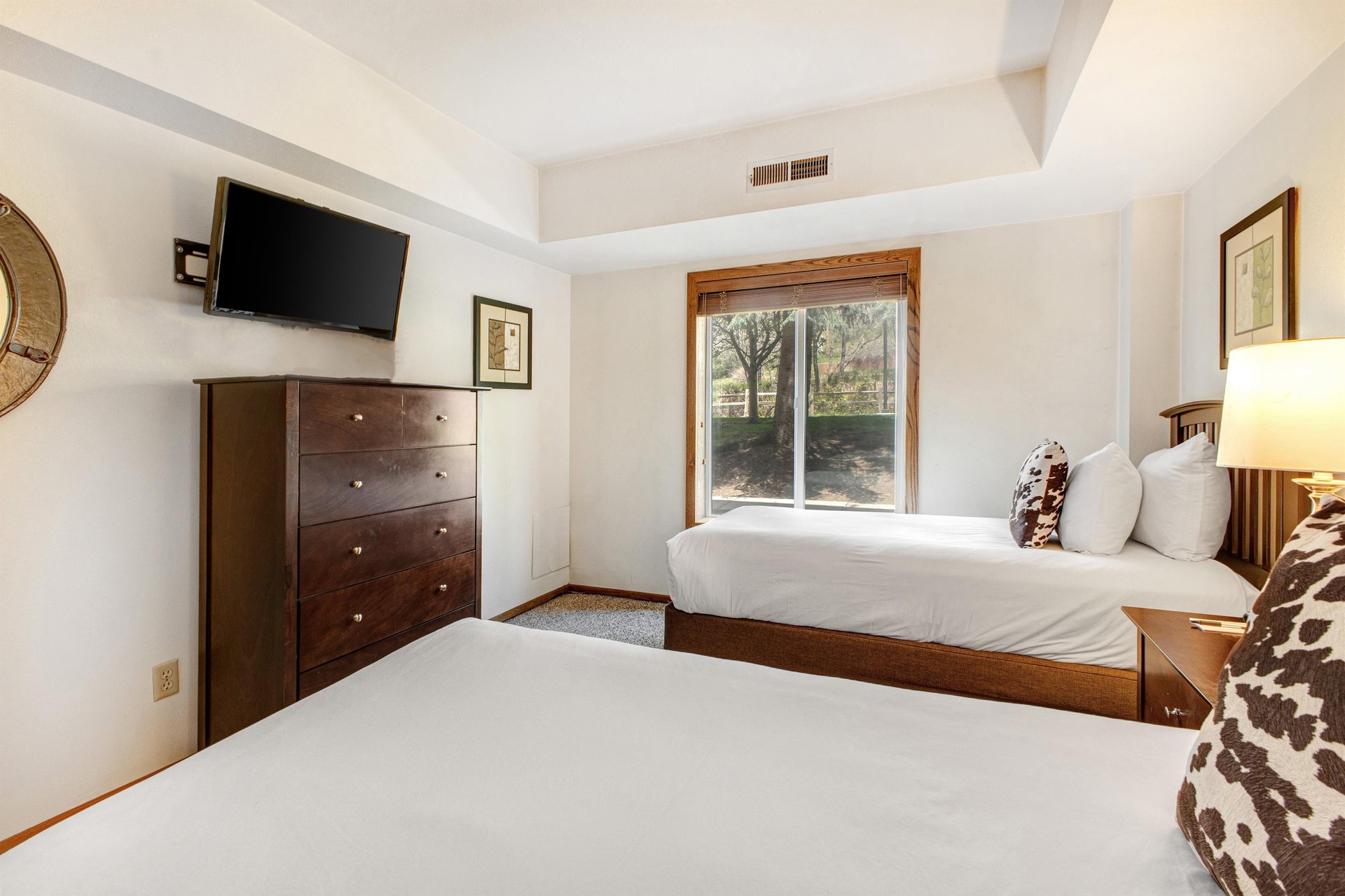 The second bedroom has two twin beds, wood dresser, and flat screen wall mounted TV.