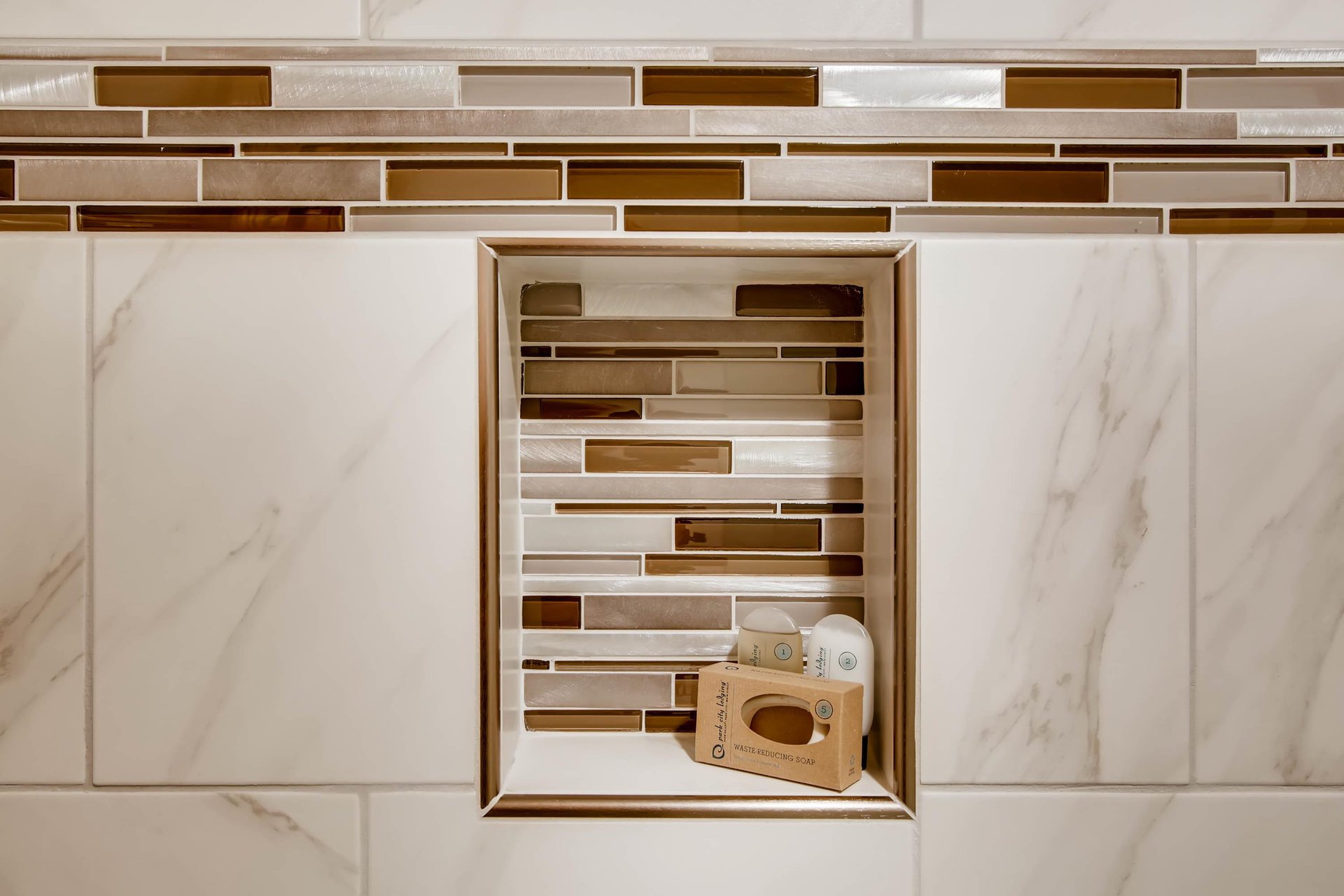 The shared bathroom has gorgeous white tile, with gold and brown decorative tile lining a shelf in the bathtub surround.